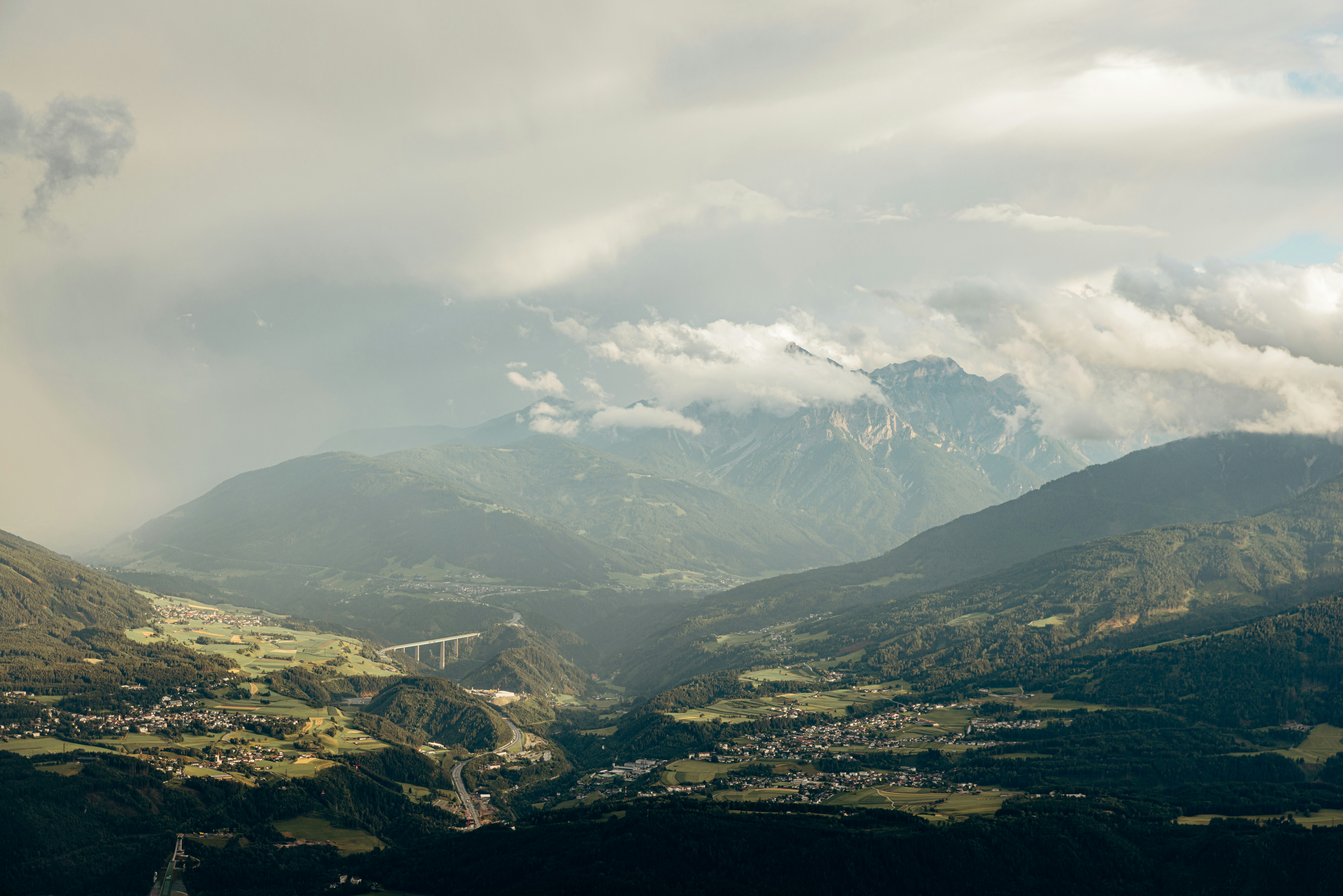 Dramatic mountain valley with clouds and a distant bridge.