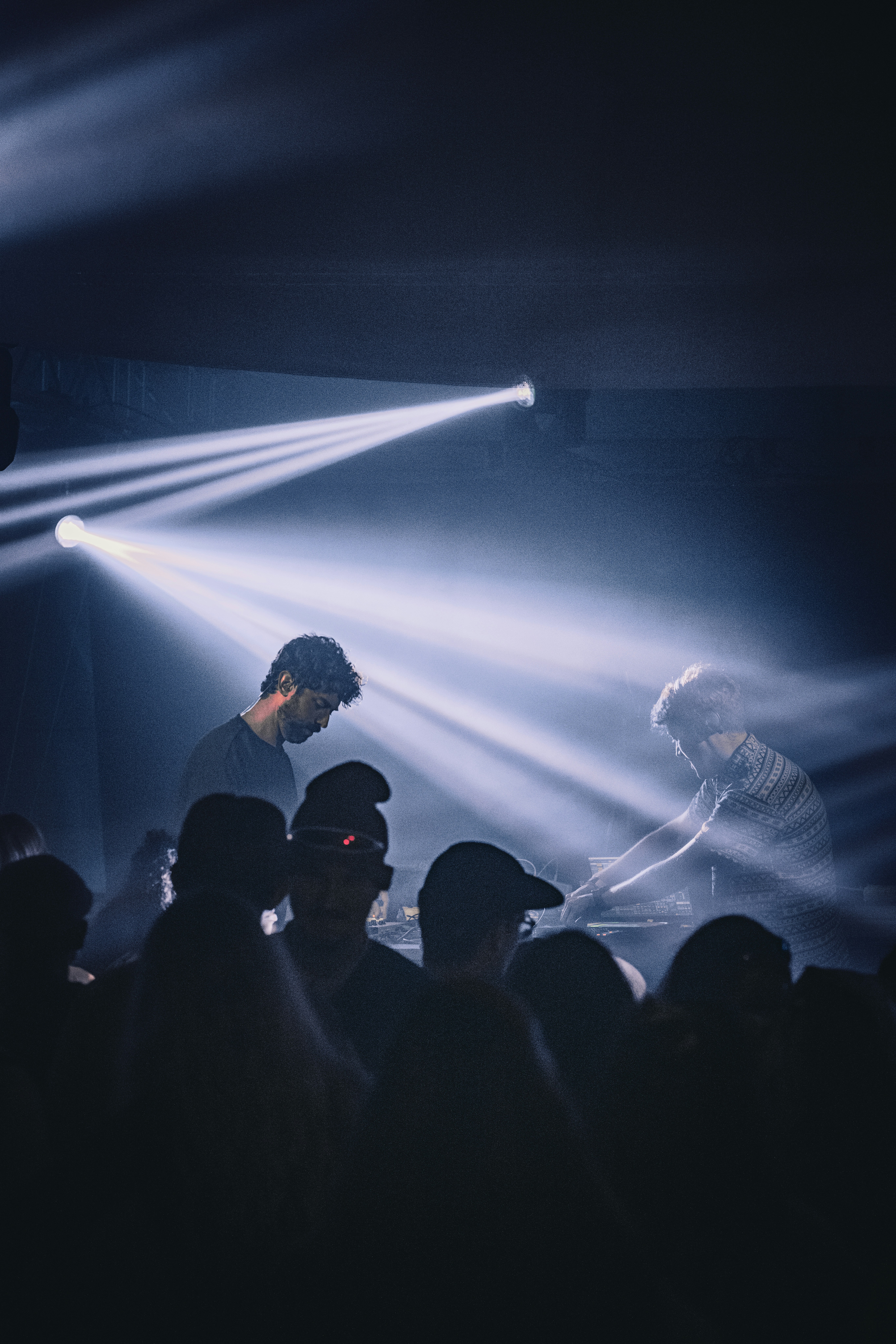Djs performing for a crowd under bright spotlights and smoke.
