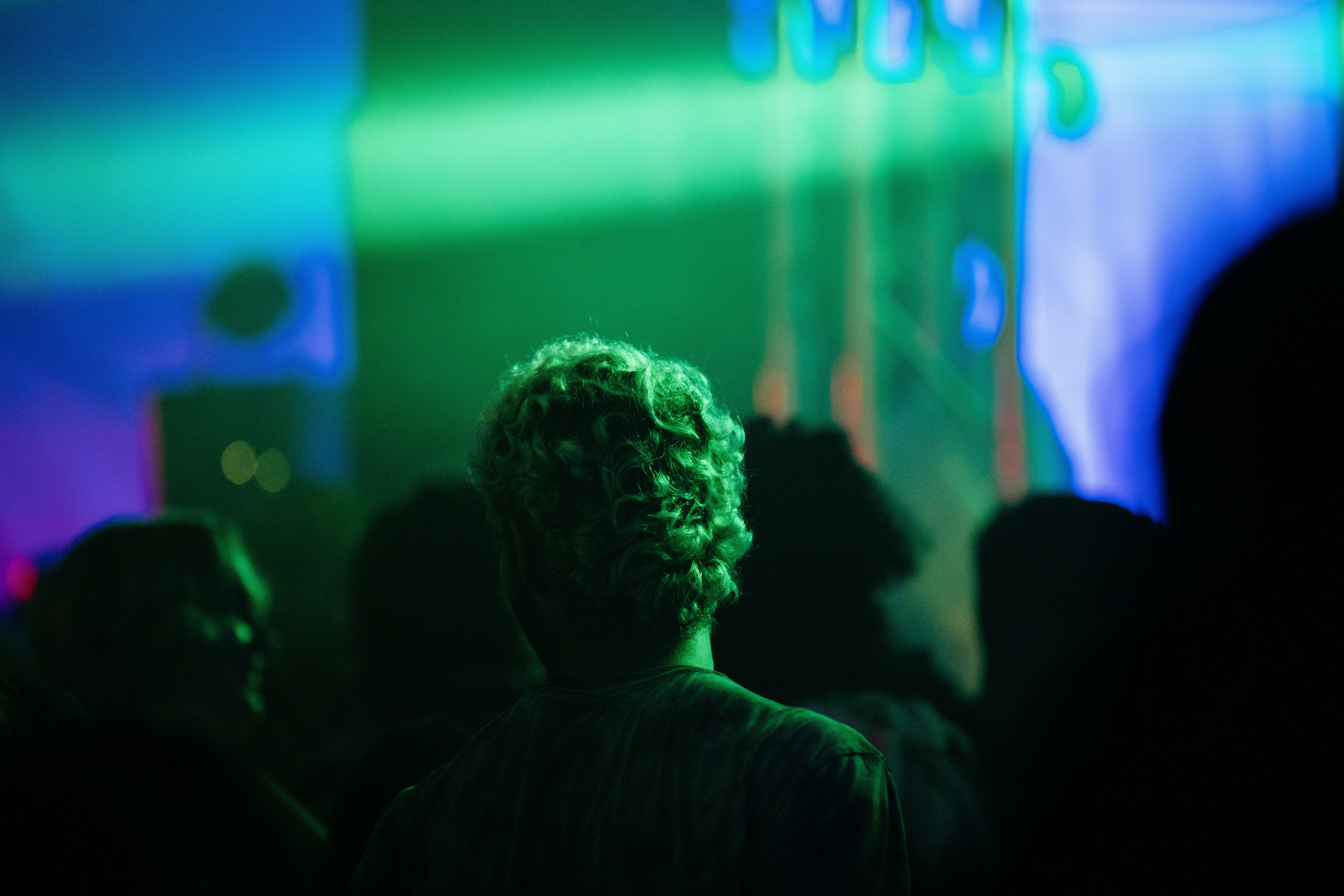 Audience member with curly hair watching a colorful light show.