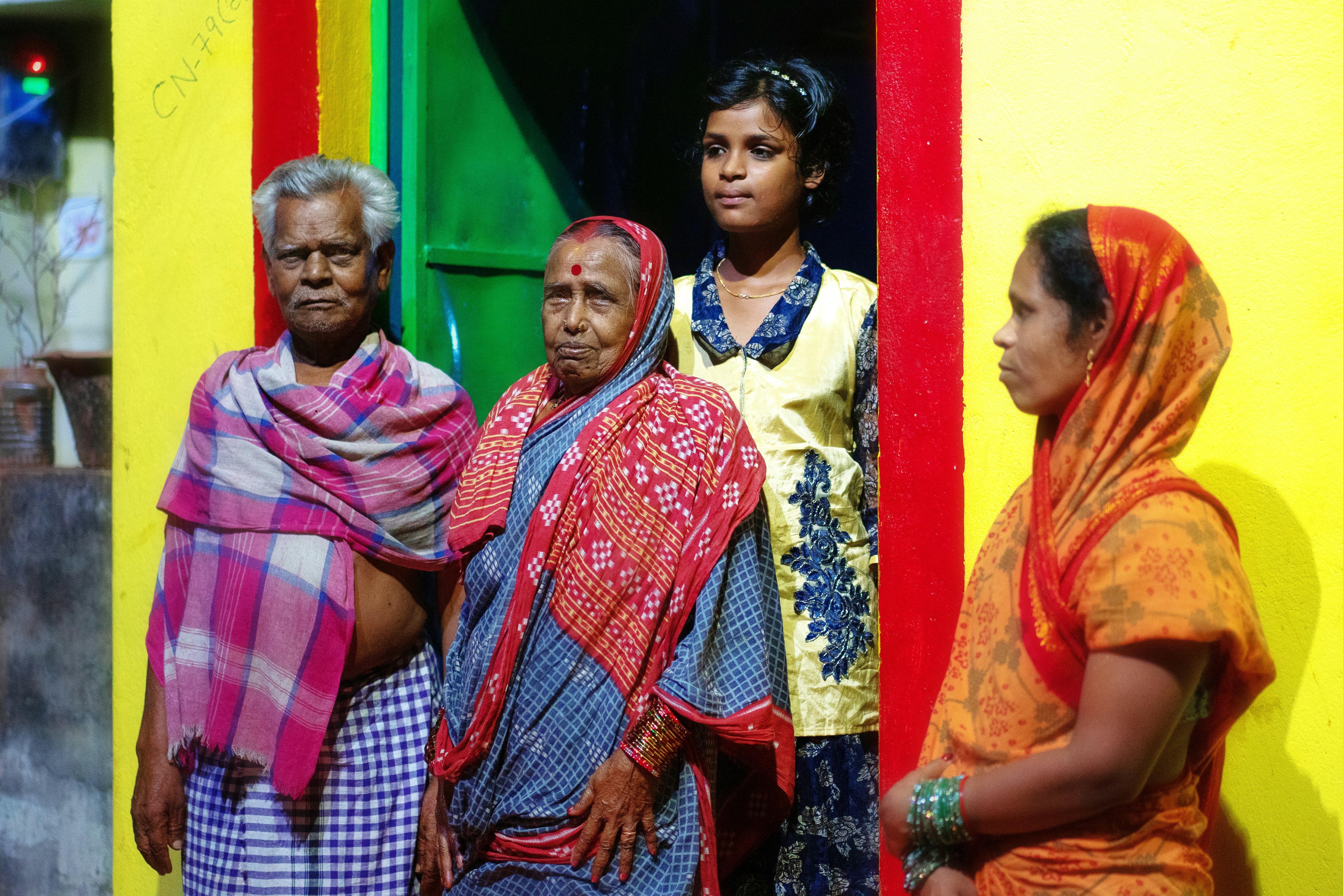 Four people in traditional attire standing by a yellow wall.
