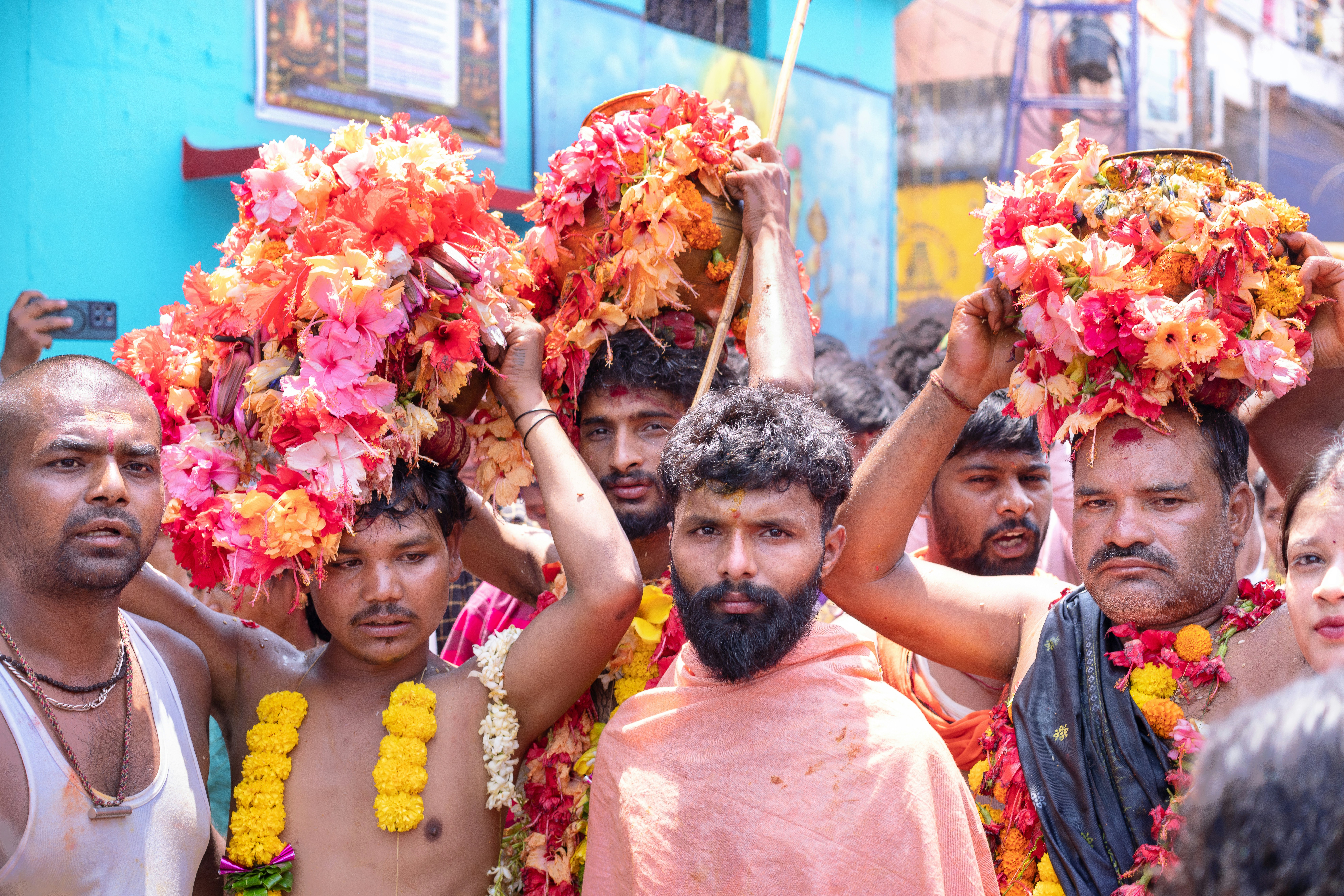 Men carry colorful flower arrangements on their heads.