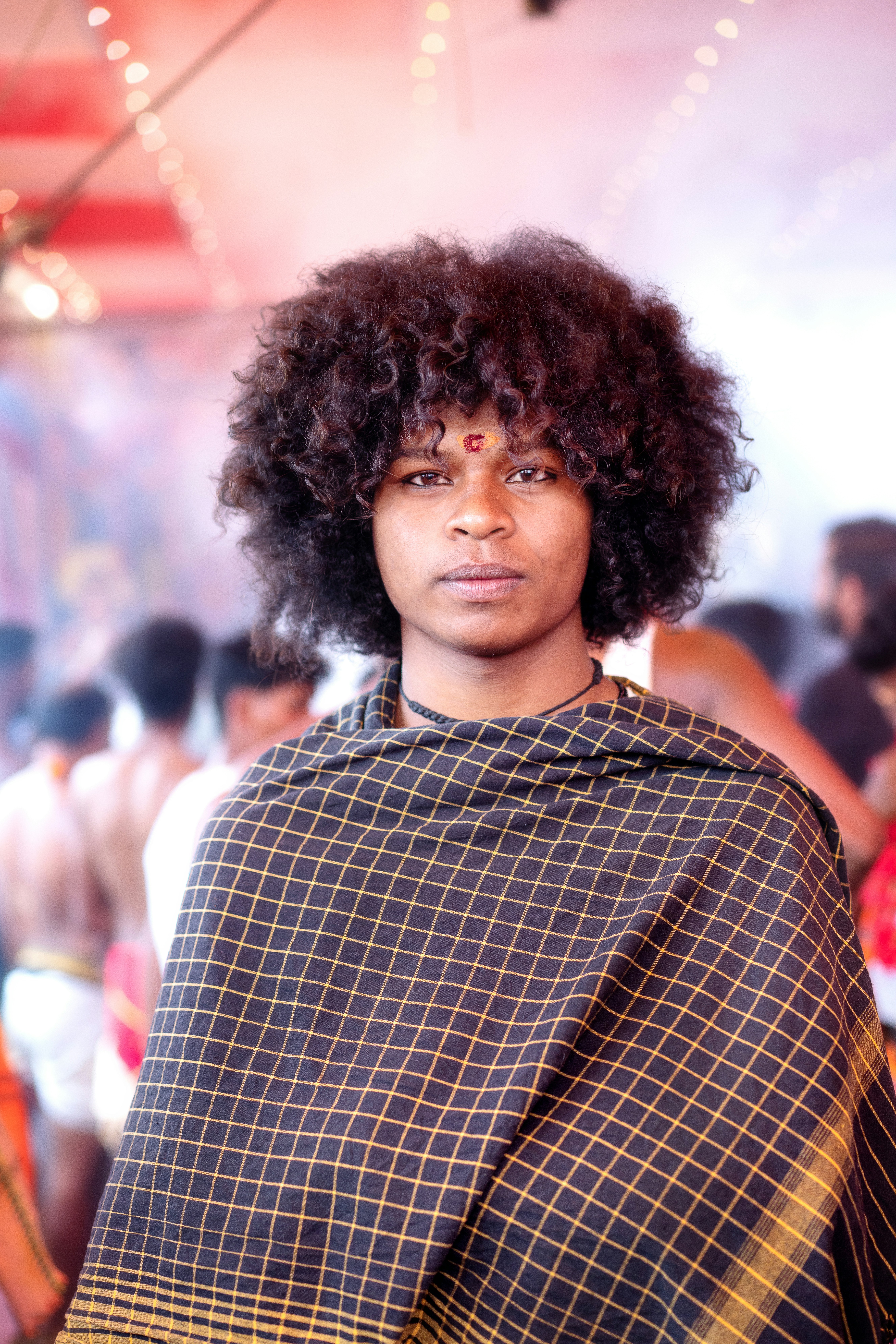 Person with curly hair and checkered shawl looking directly.
