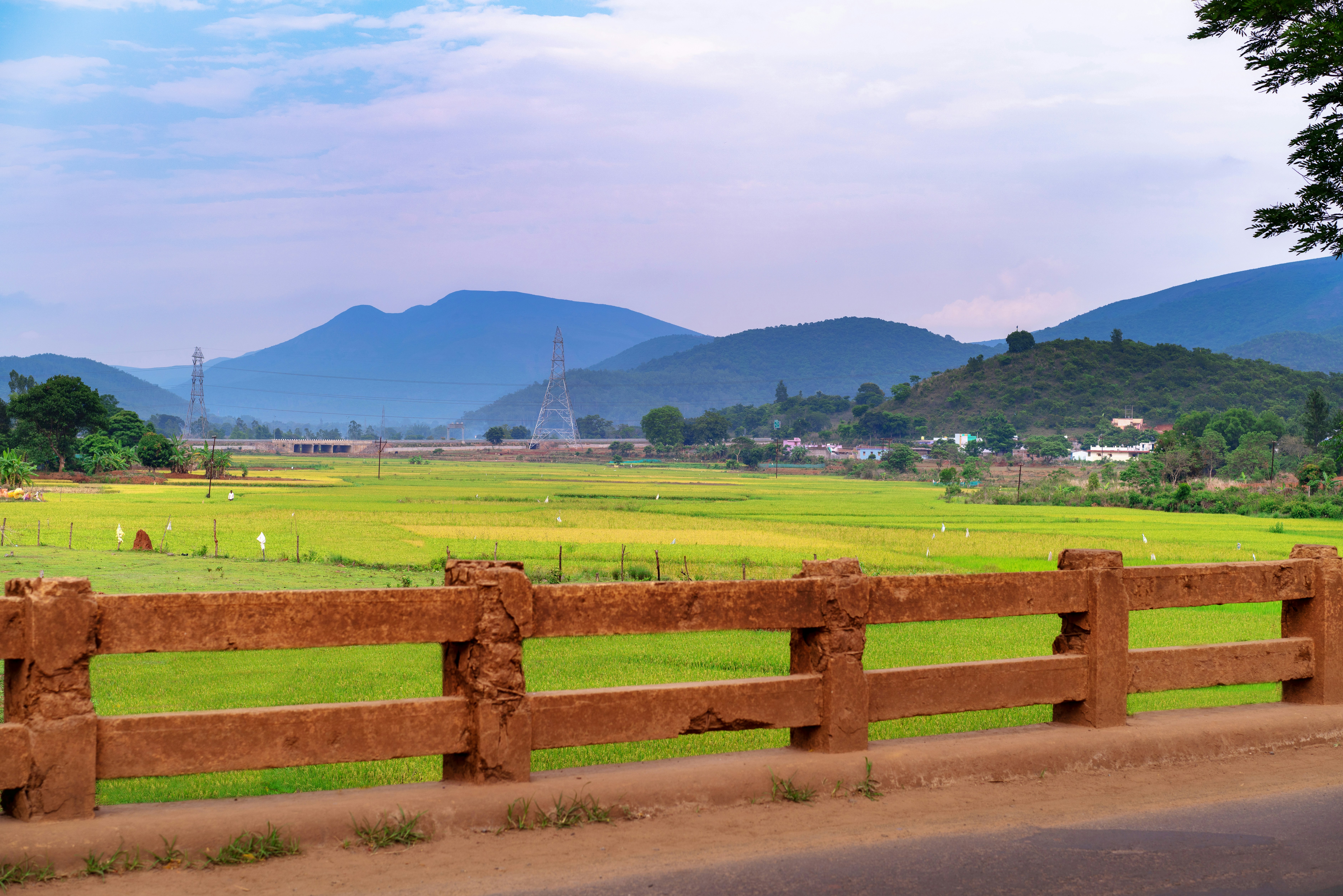 A brown fence overlooks green fields and distant blue mountains.