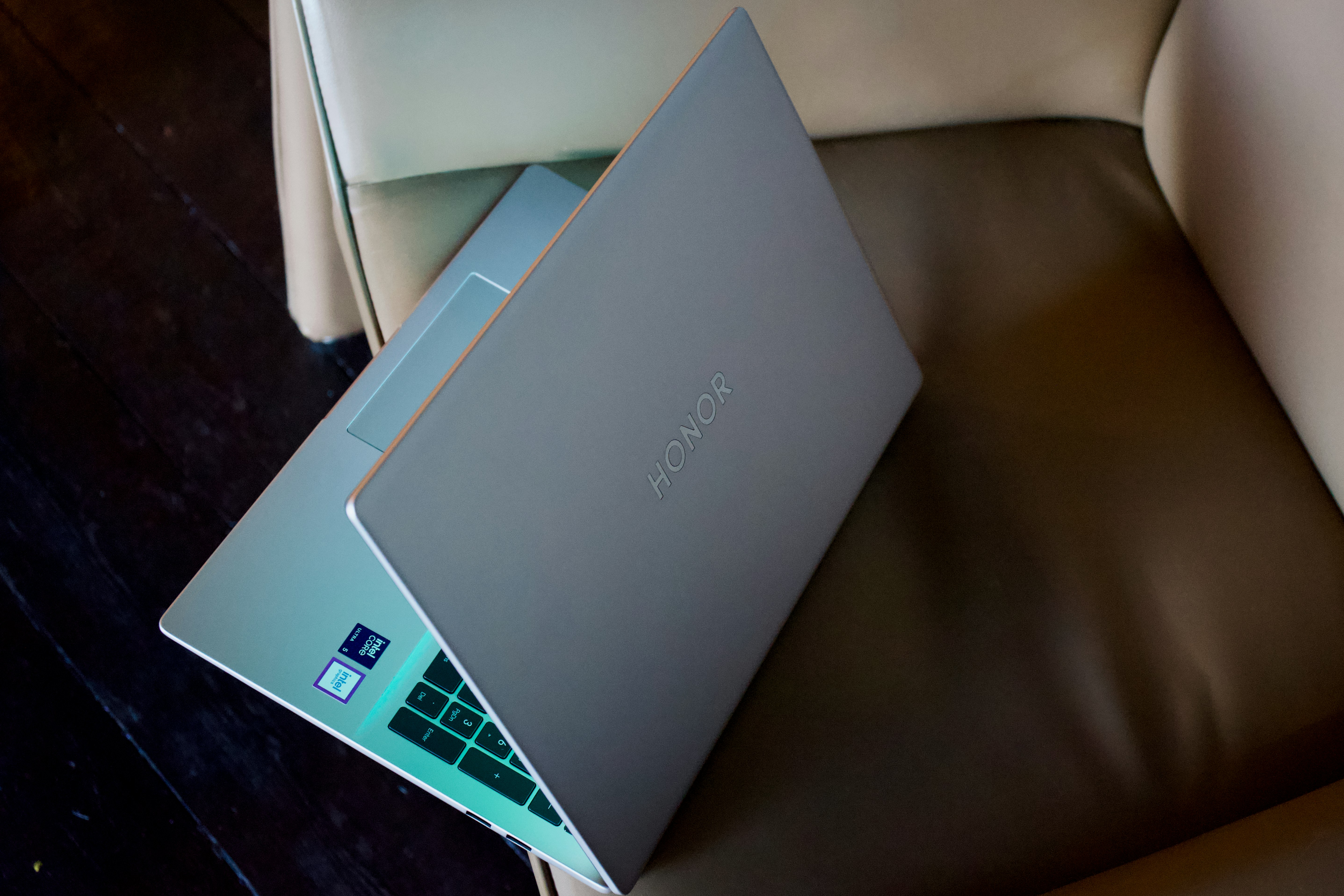 A silver laptop rests partially open on a brown chair.