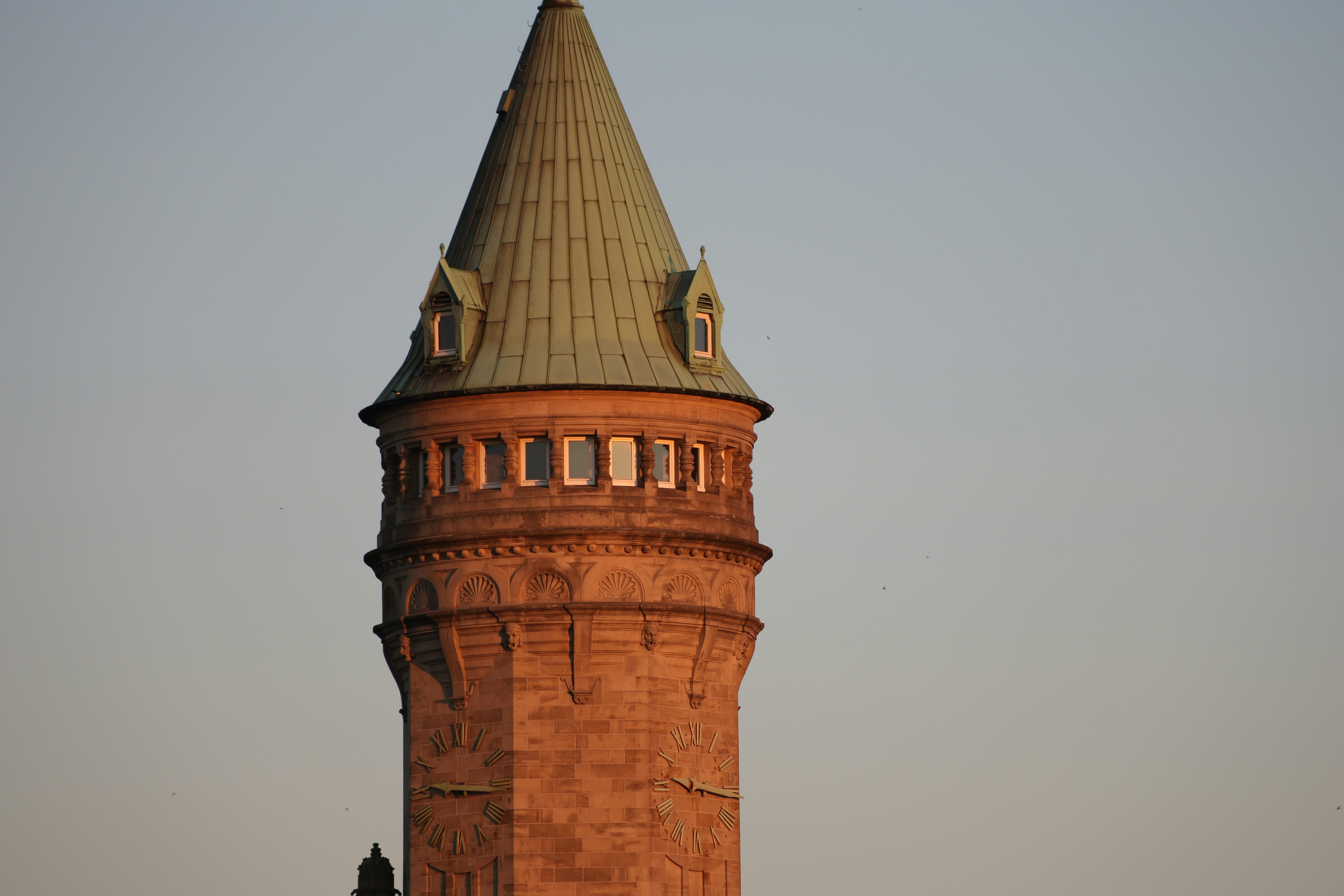 An old stone tower with a green roof at sunset.
