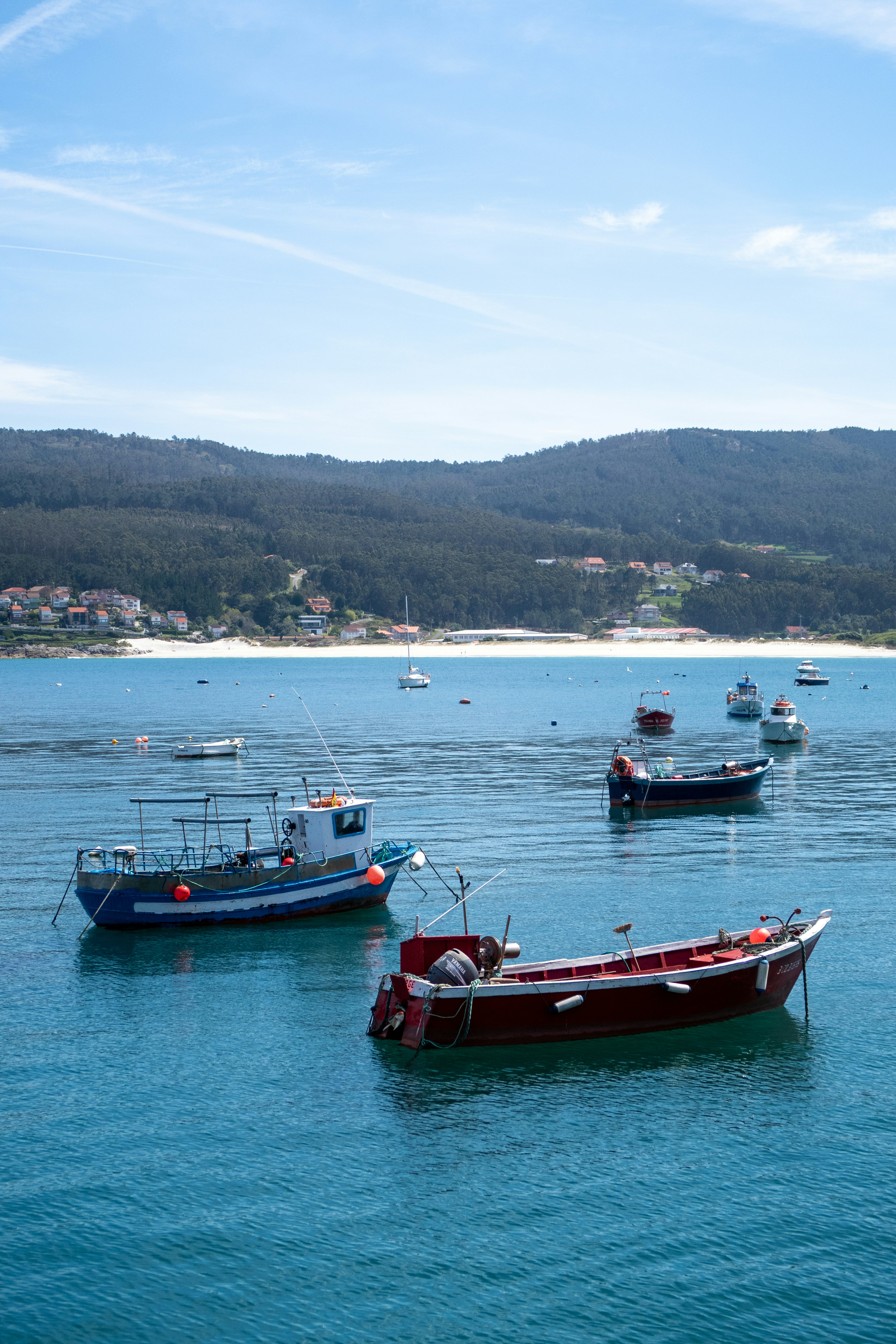 Boats on blue water with a beach and forested hills.