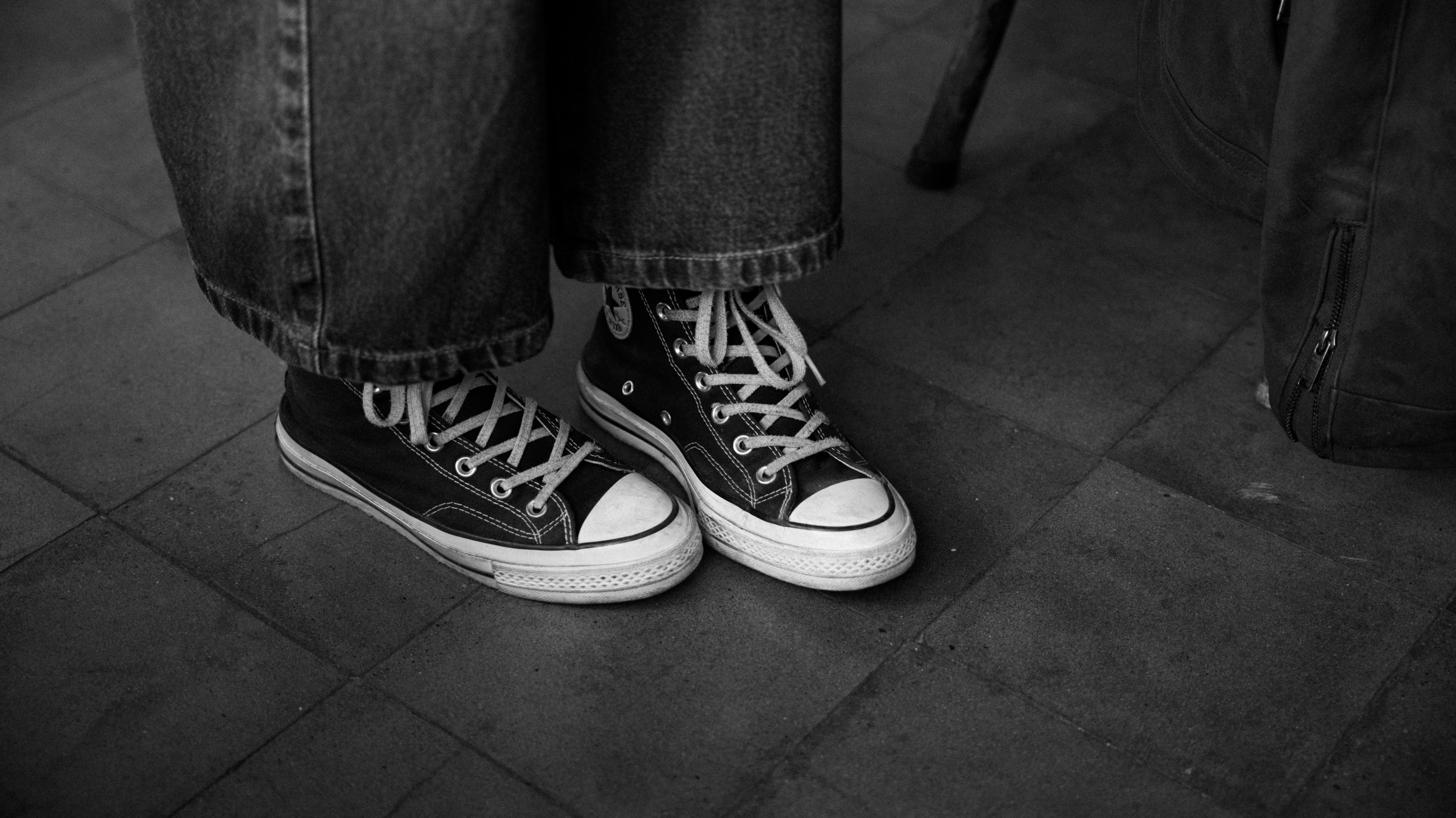 Person wearing black sneakers and jeans on a tiled floor.