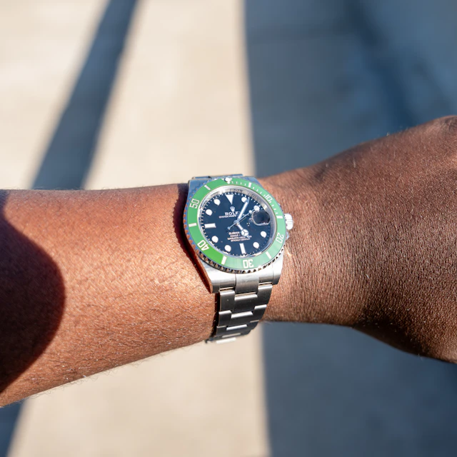 A wrist wearing a stainless steel Rolex dive watch with a green bezel