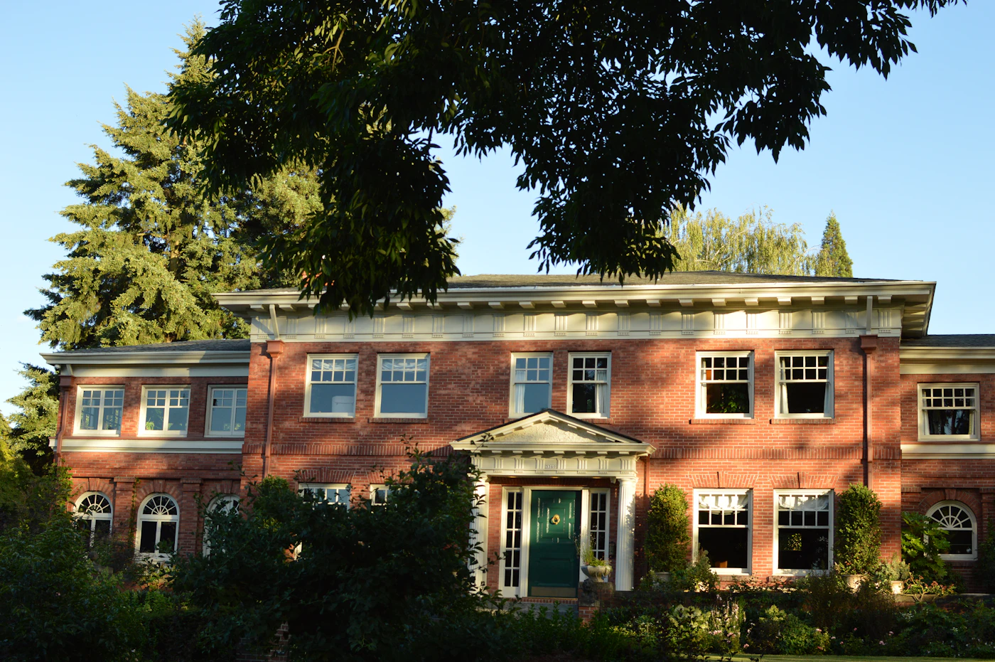 Brick two-story house with a green front door behind trees
