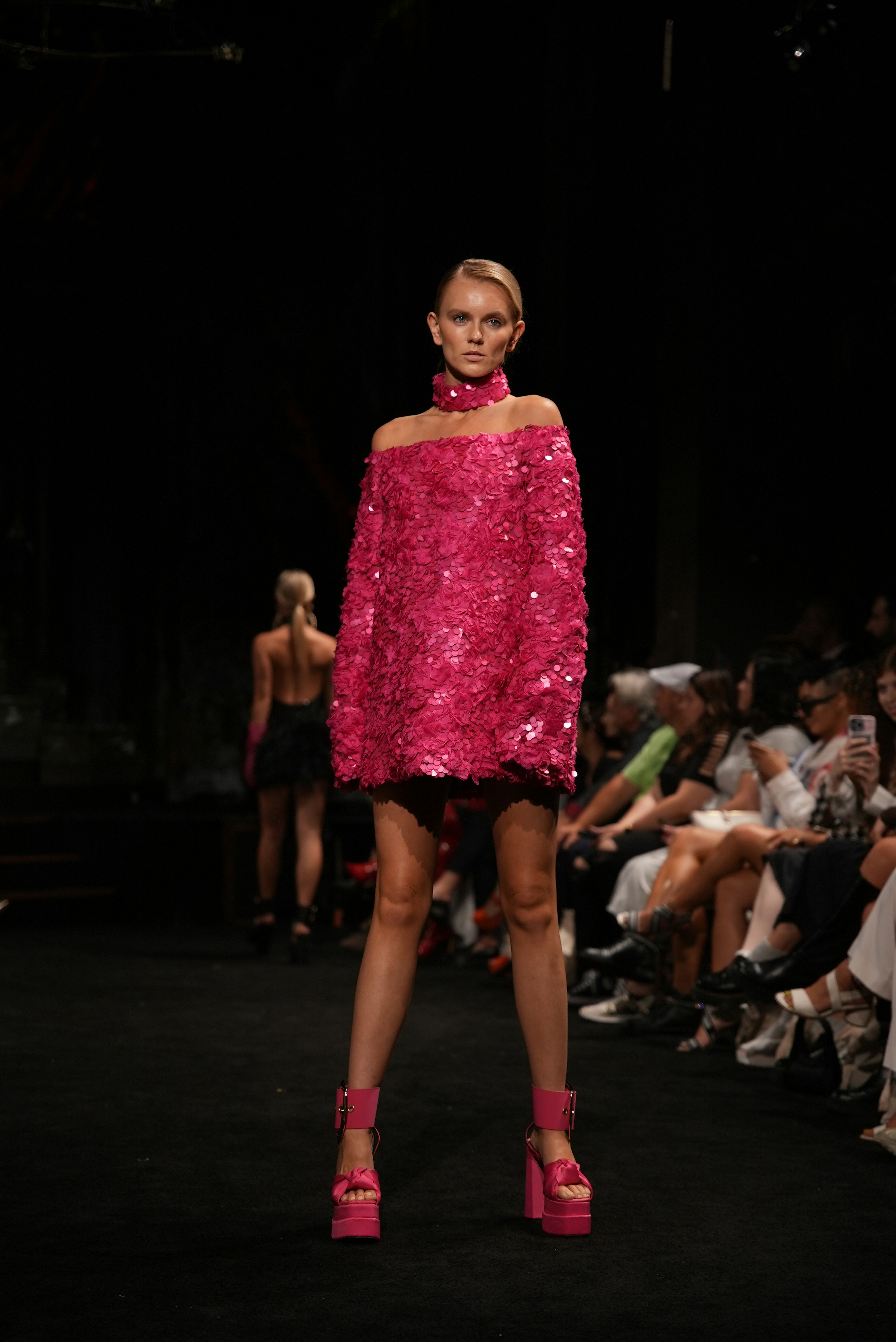 Blonde model in a pink sequined off-shoulder dress on runway.