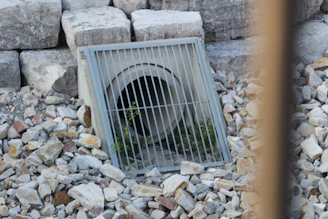 A storm drain with a metal grate surrounded by rocks