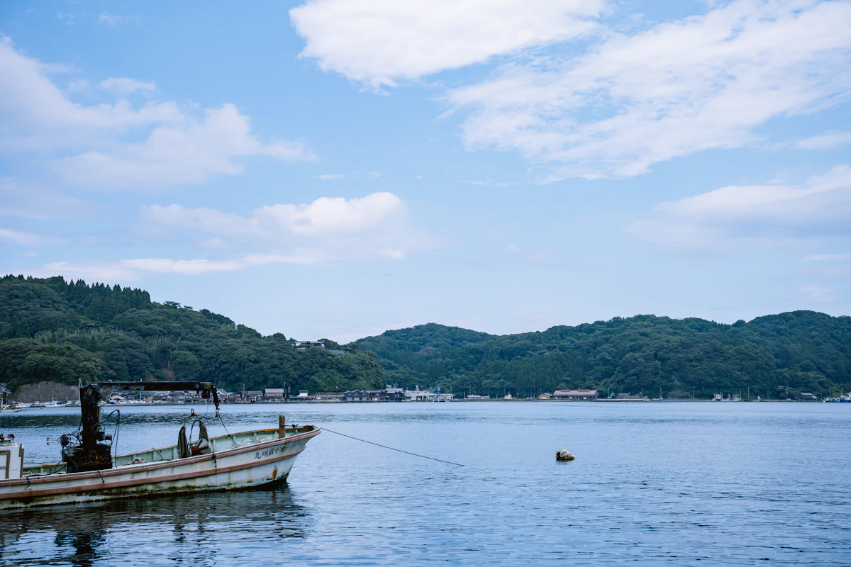 An old fishing boat in the calm water of Ine Bay with green hills behind