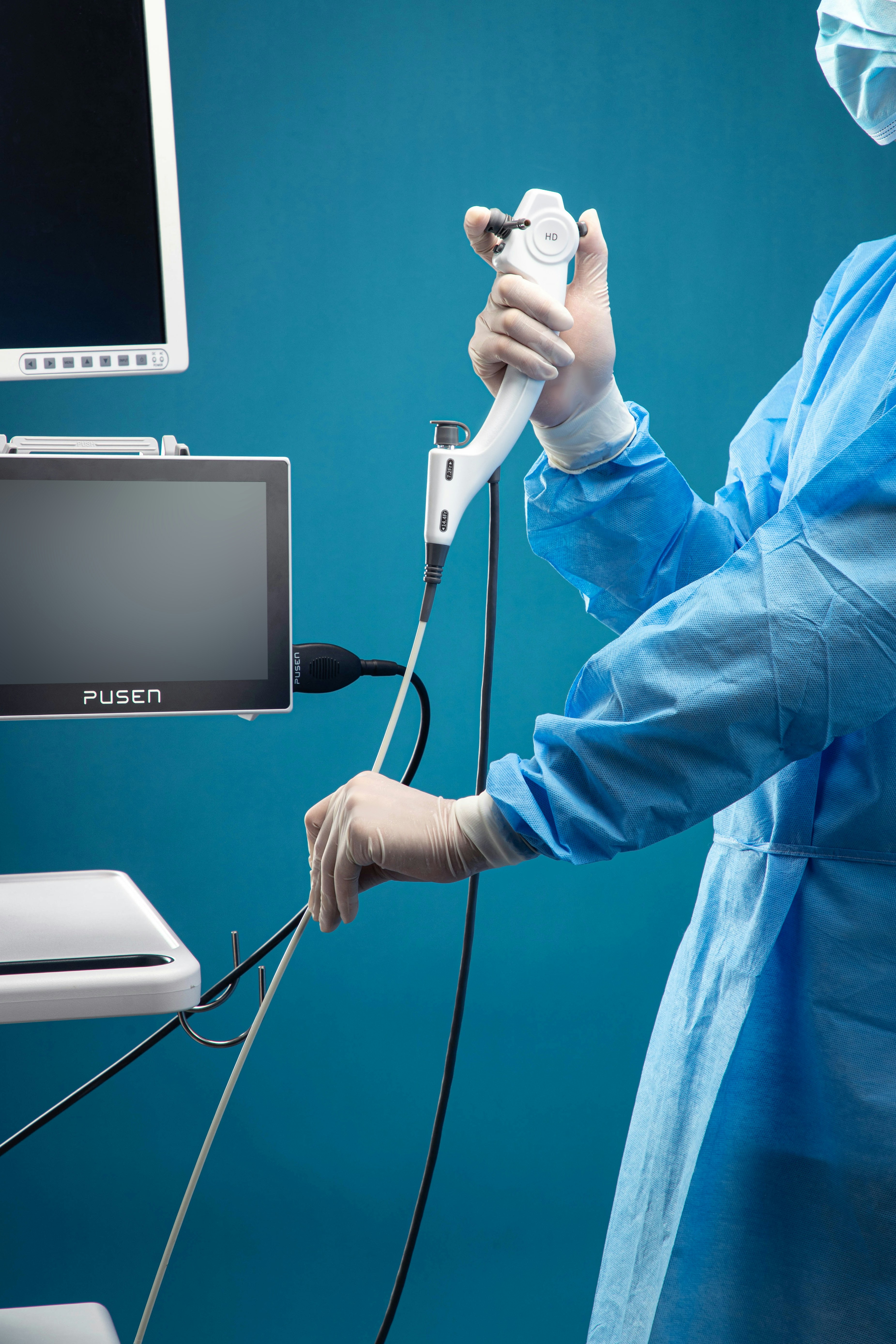 A person in a blue surgical gown holding a medical endoscope near a monitor