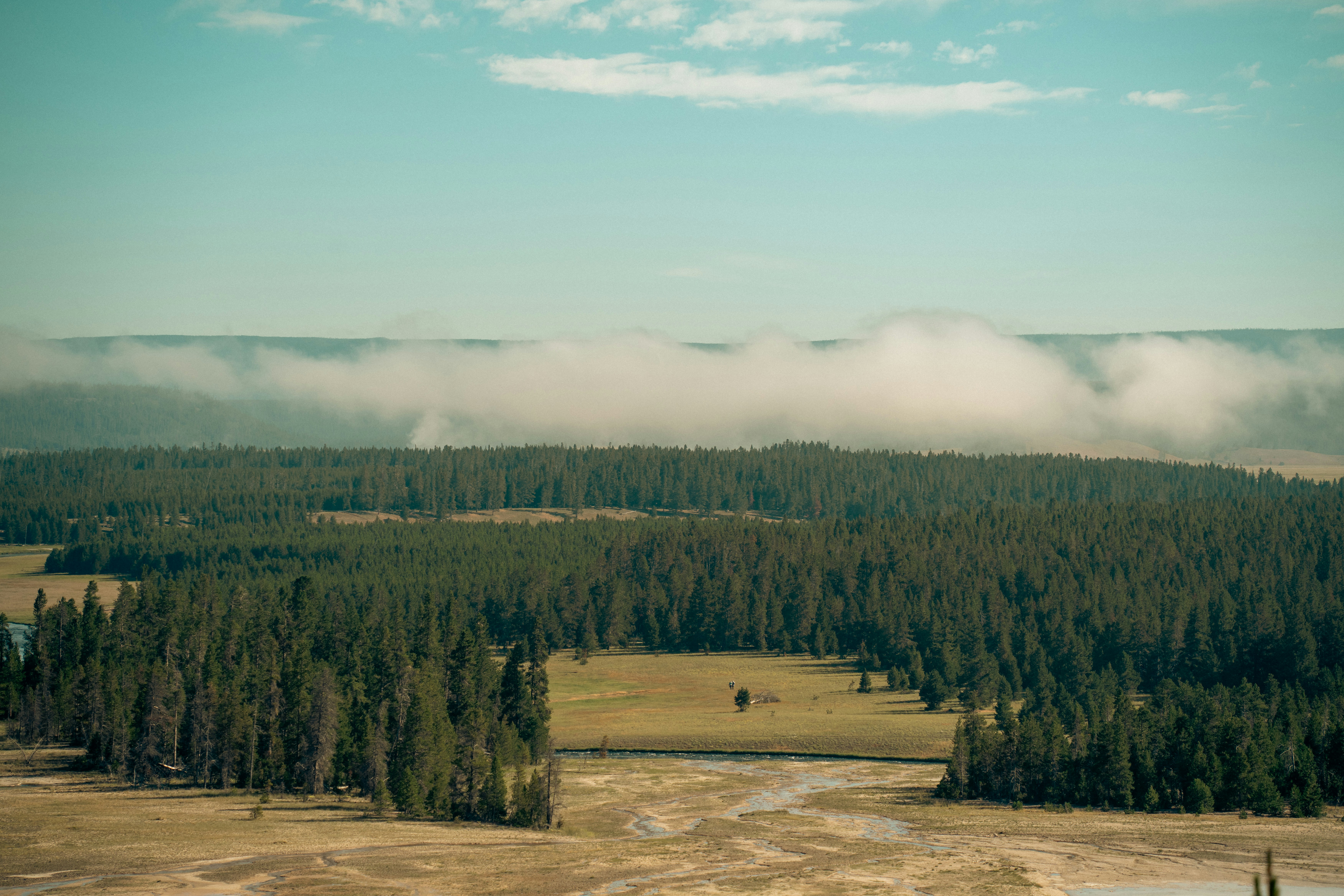 Vibrant, multi-colored thermal pools (like Grand Prismatic) steaming under a wide sky, seen from an elevated boardwalk.