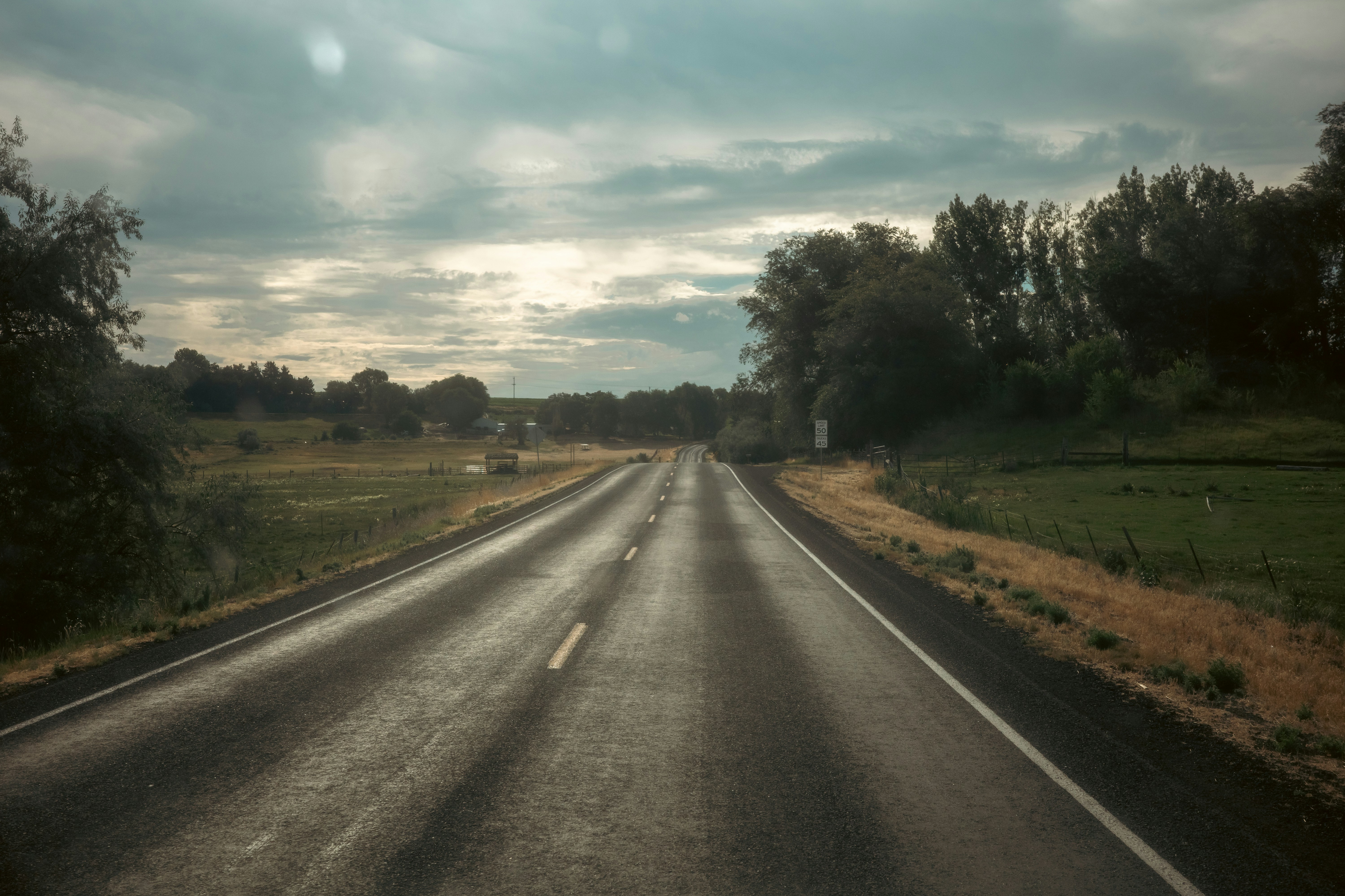 Estrada vazia por uma paisagem rural sob um céu nublado e dramático.