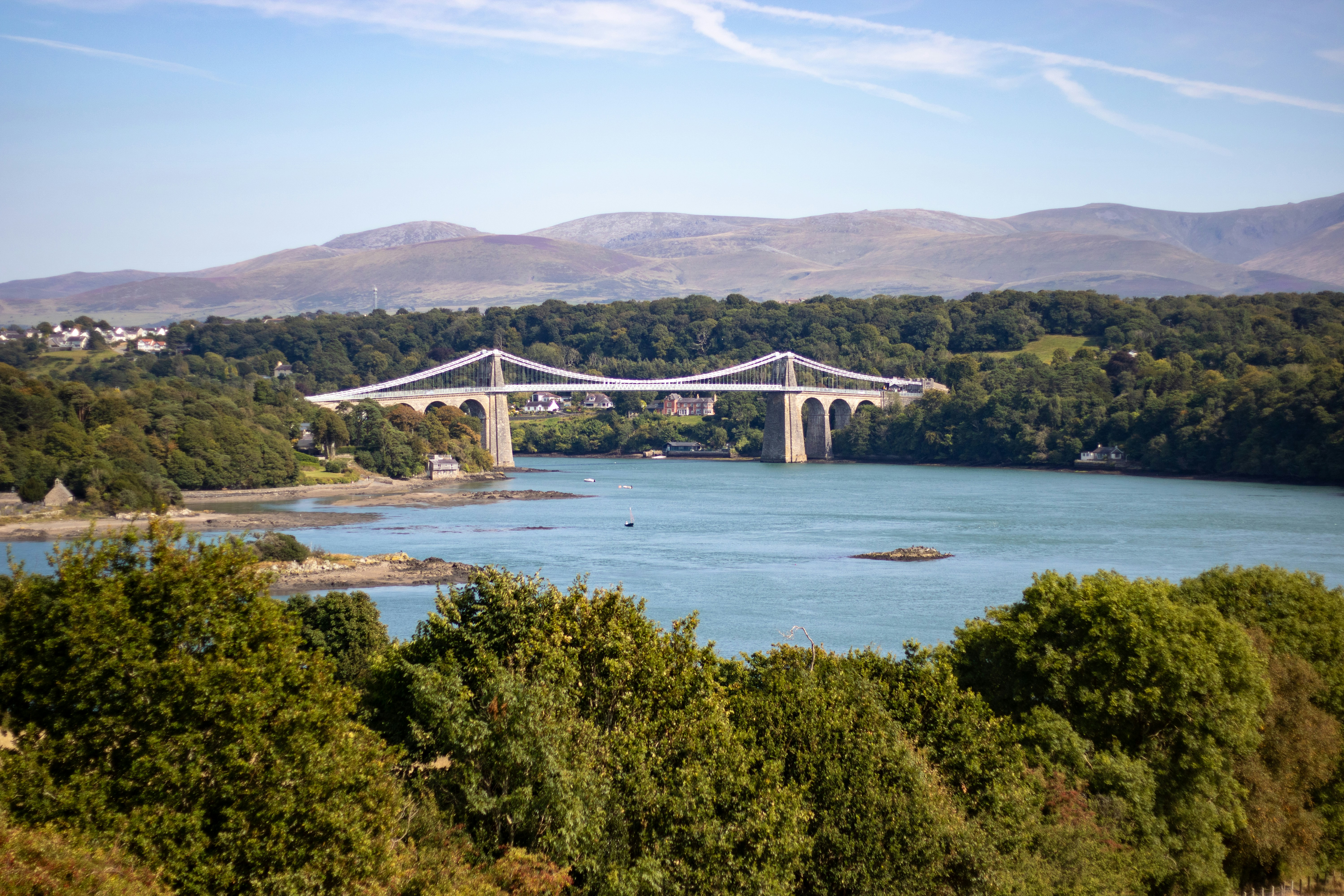Die historische Hängebrücke überspannt einen ruhigen Fluss mit fernen Bergen