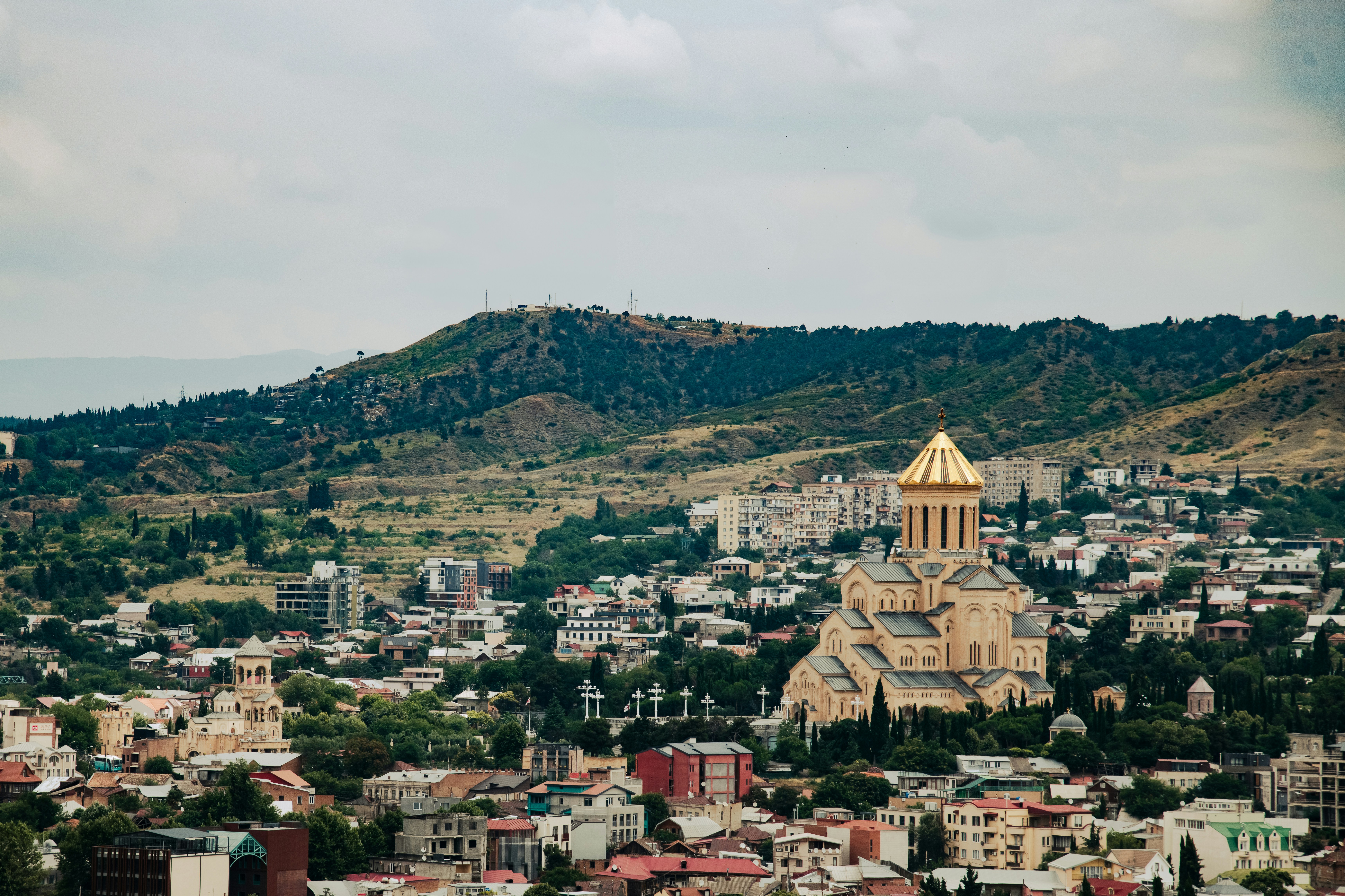 Tbilisi cityscape with a golden-domed cathedral and distant hills.