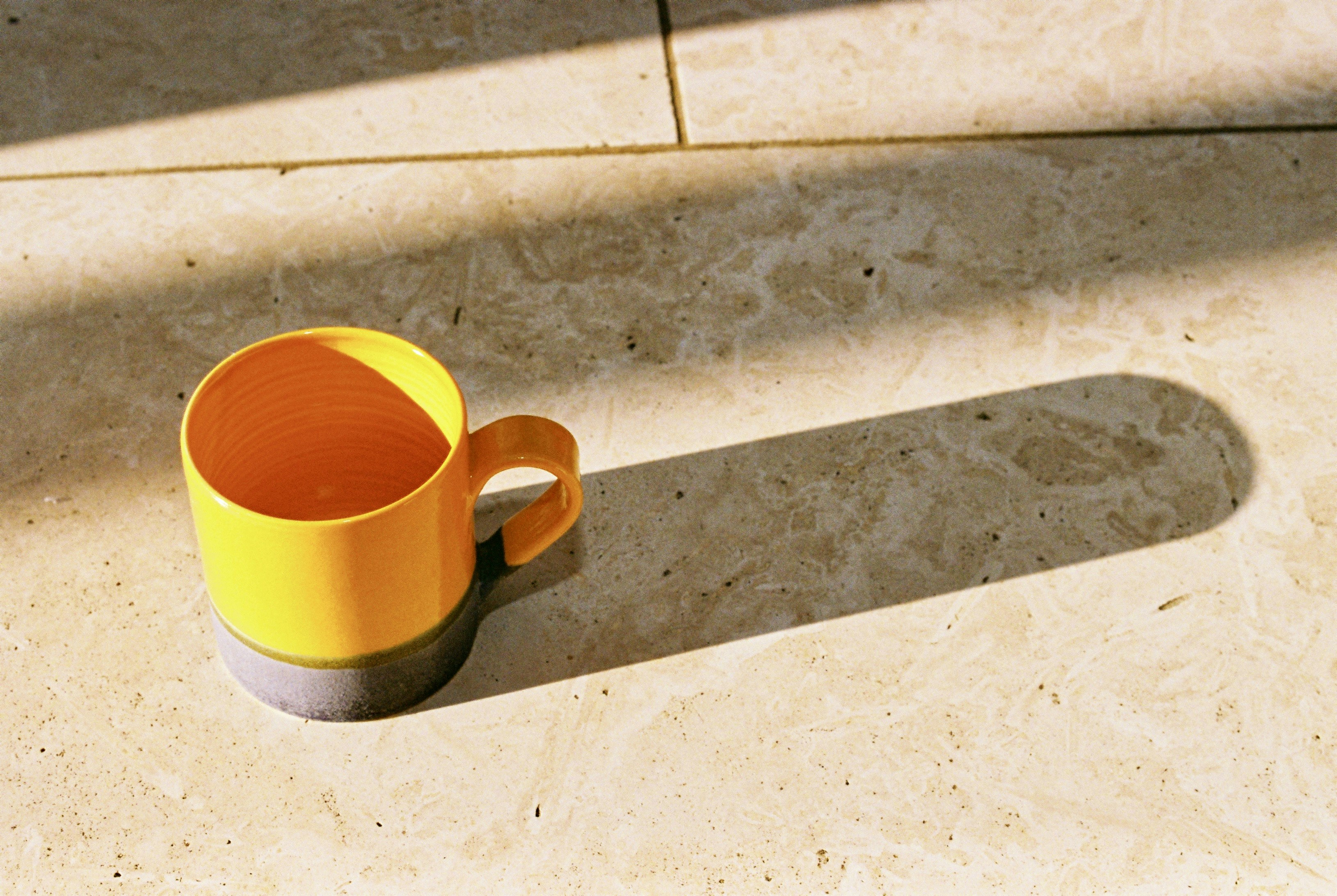 Yellow mug casting long shadow on tiled floor