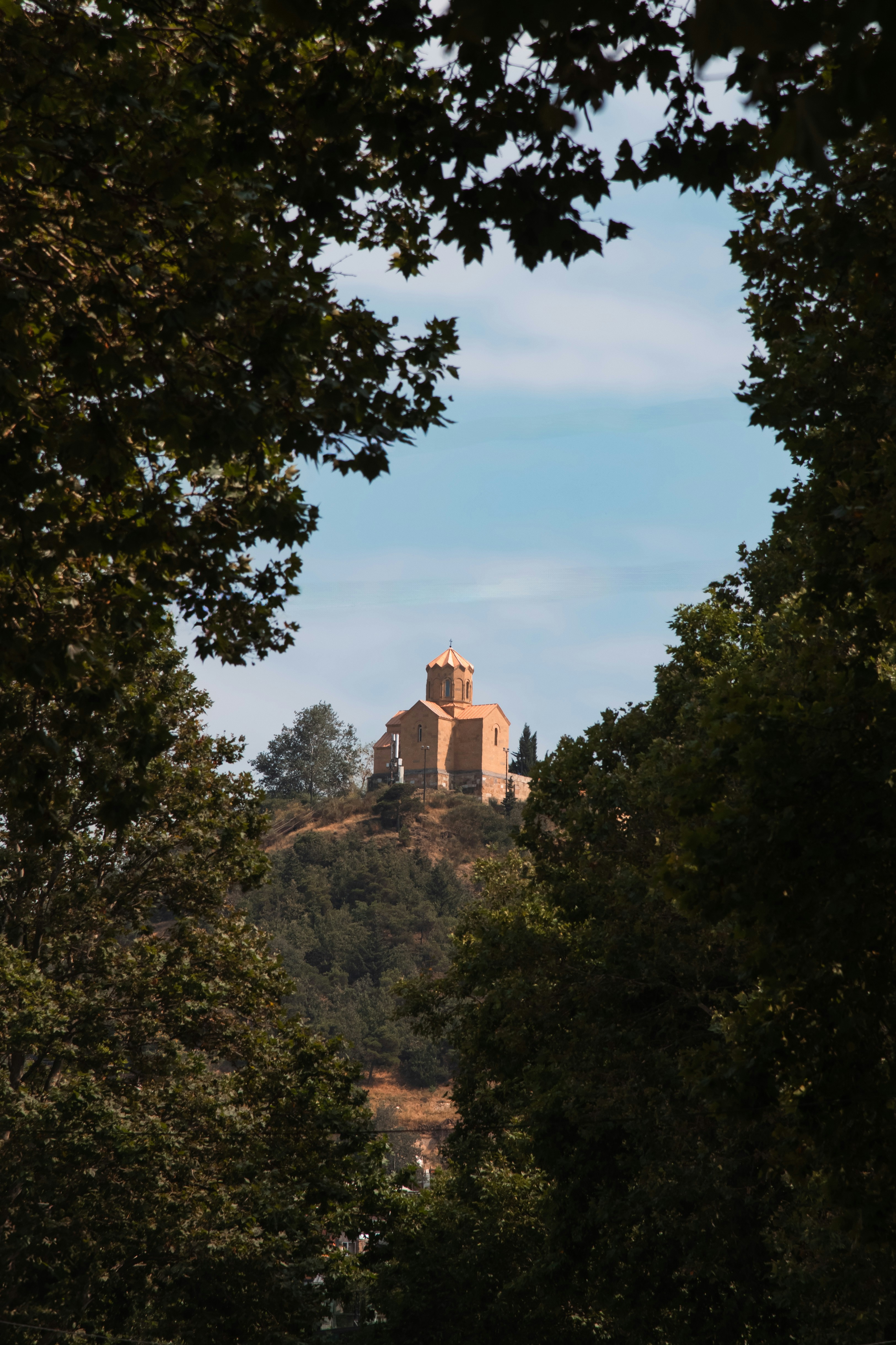 Igreja antiga de pedra em uma colina emoldurada por árvores verdes.