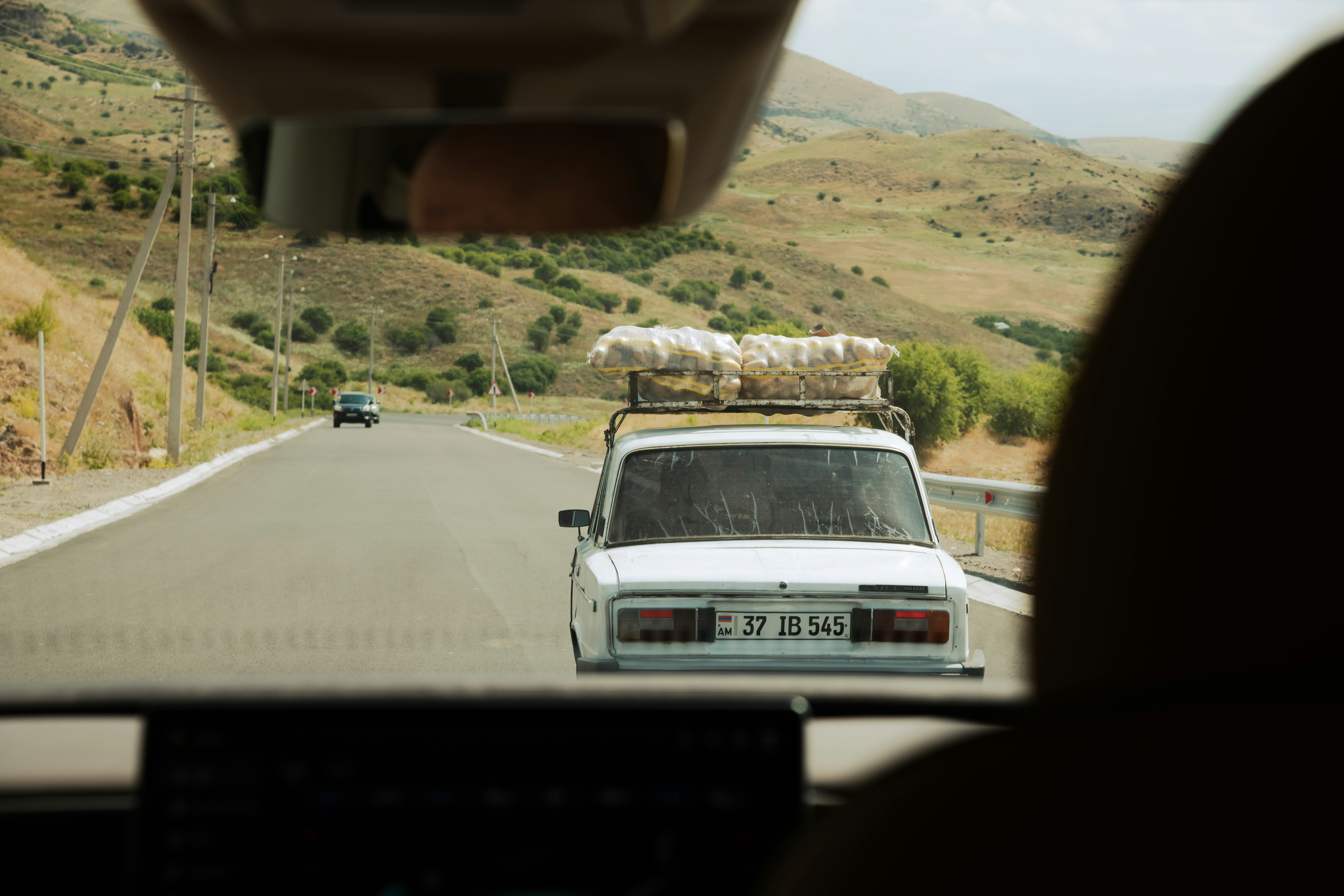 Carro branco com carga no teto em uma estrada rural sinuosa.