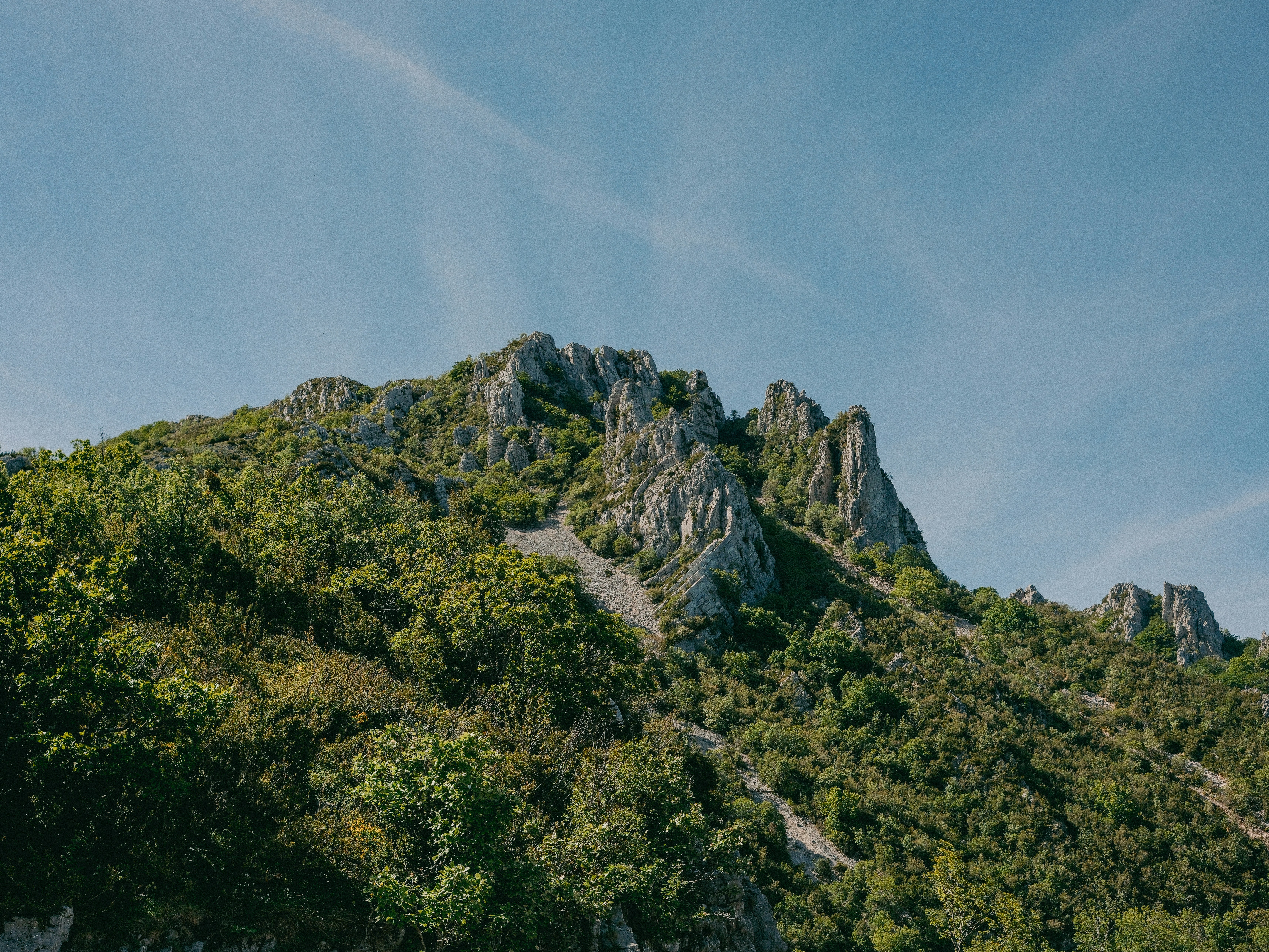 青空の下、岩だらけの峰が広がる緑の山。