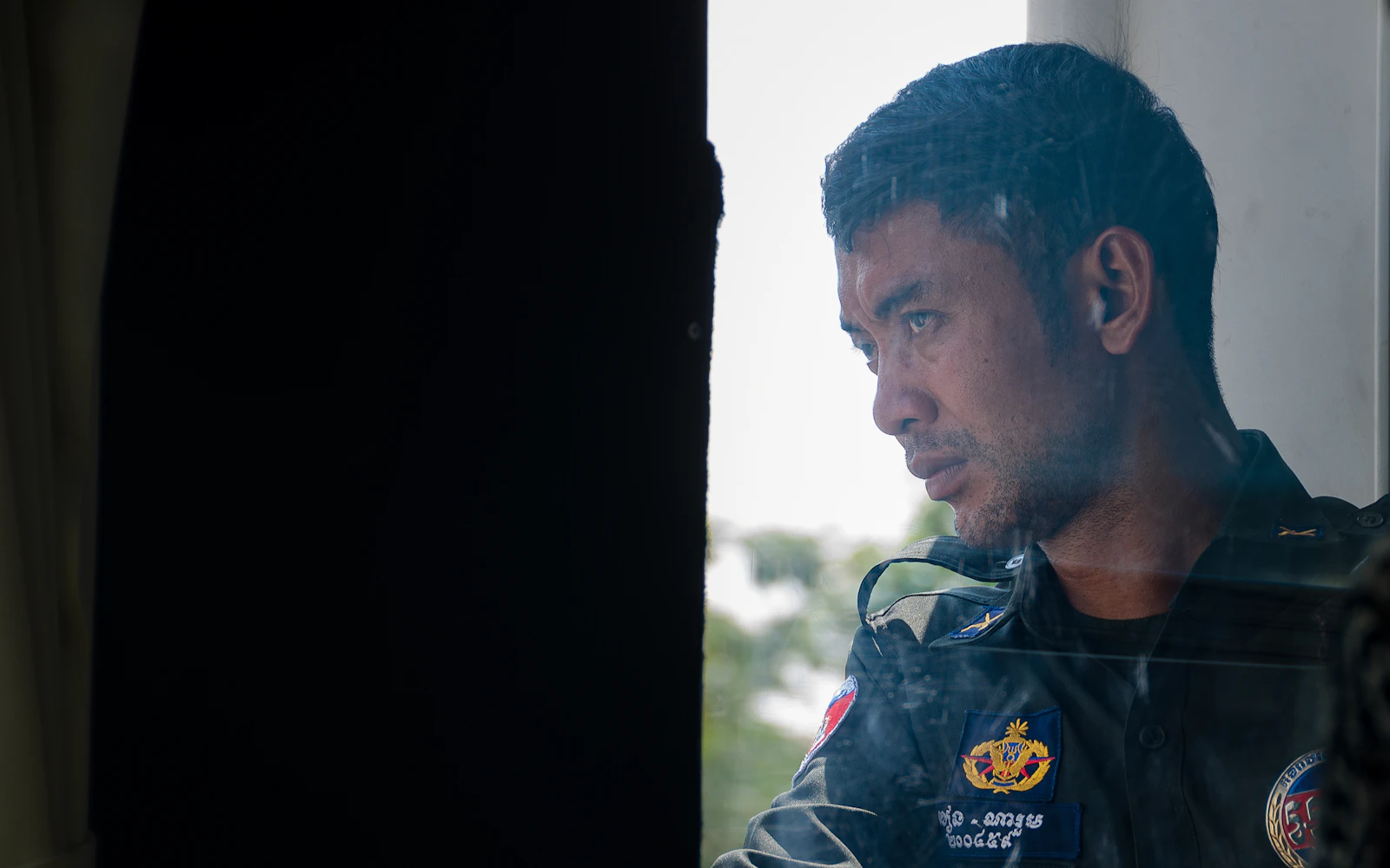Officer in uniform watching from a dark window