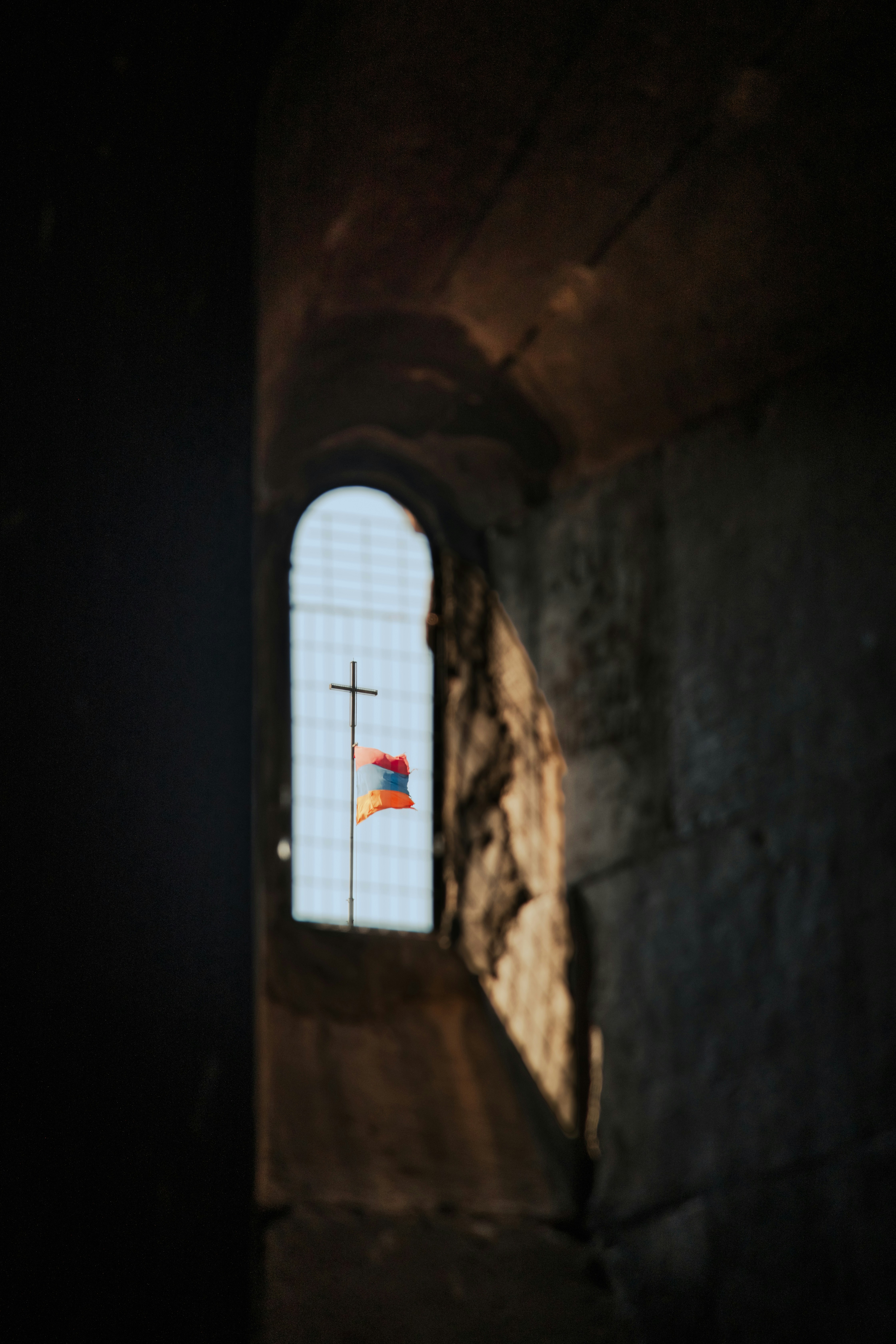 A luz do sol entrando por uma janela arqueada revelando uma cruz e uma bandeira.