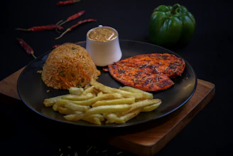 Grilled chicken, rice, fries, and sauce on a dark plate