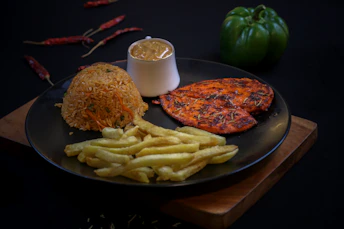 Grilled chicken, rice, fries, and sauce on a dark plate