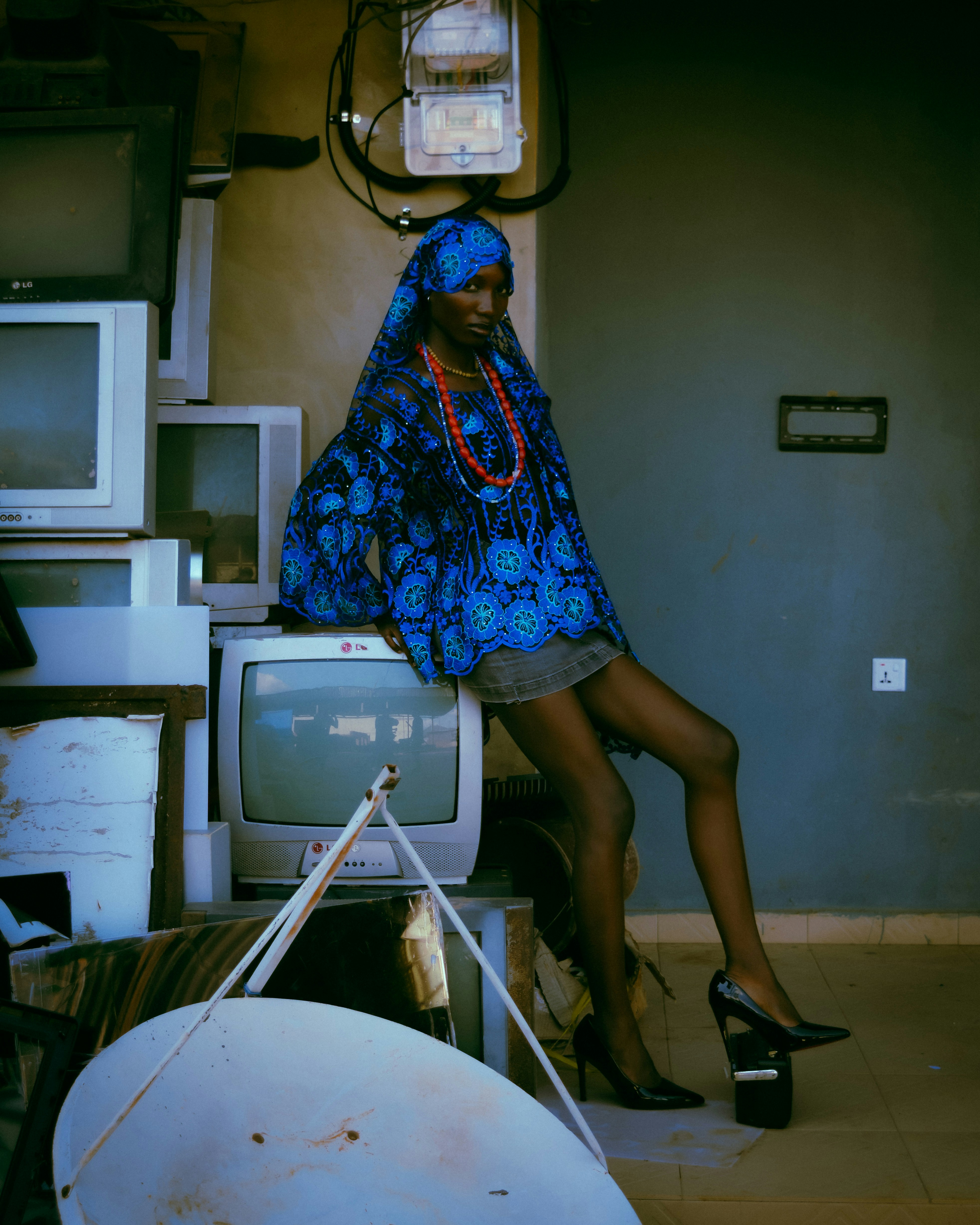 Stylish person in blue poses with stack of vintage televisions