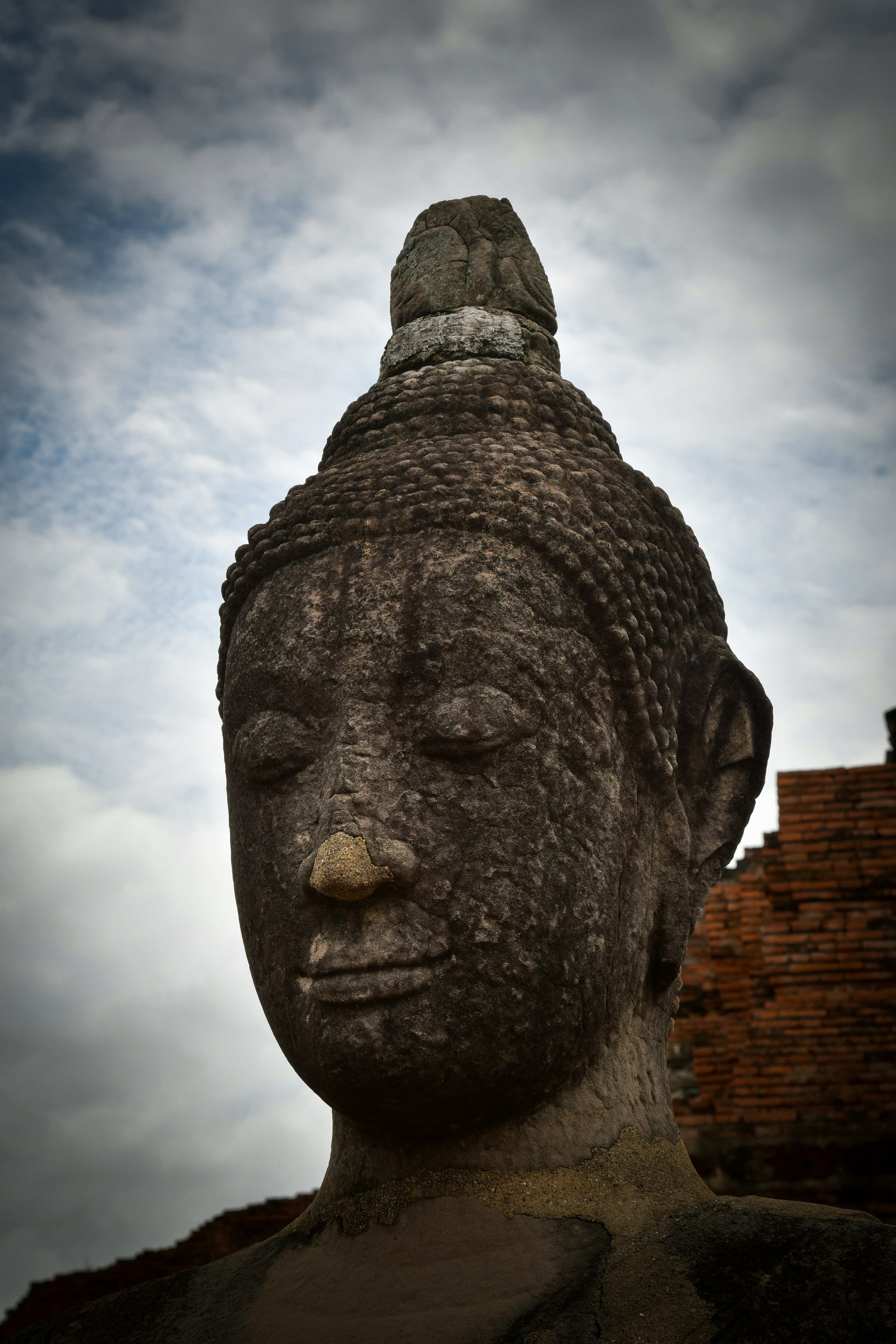 Weathered stone buddha statue against a cloudy sky.