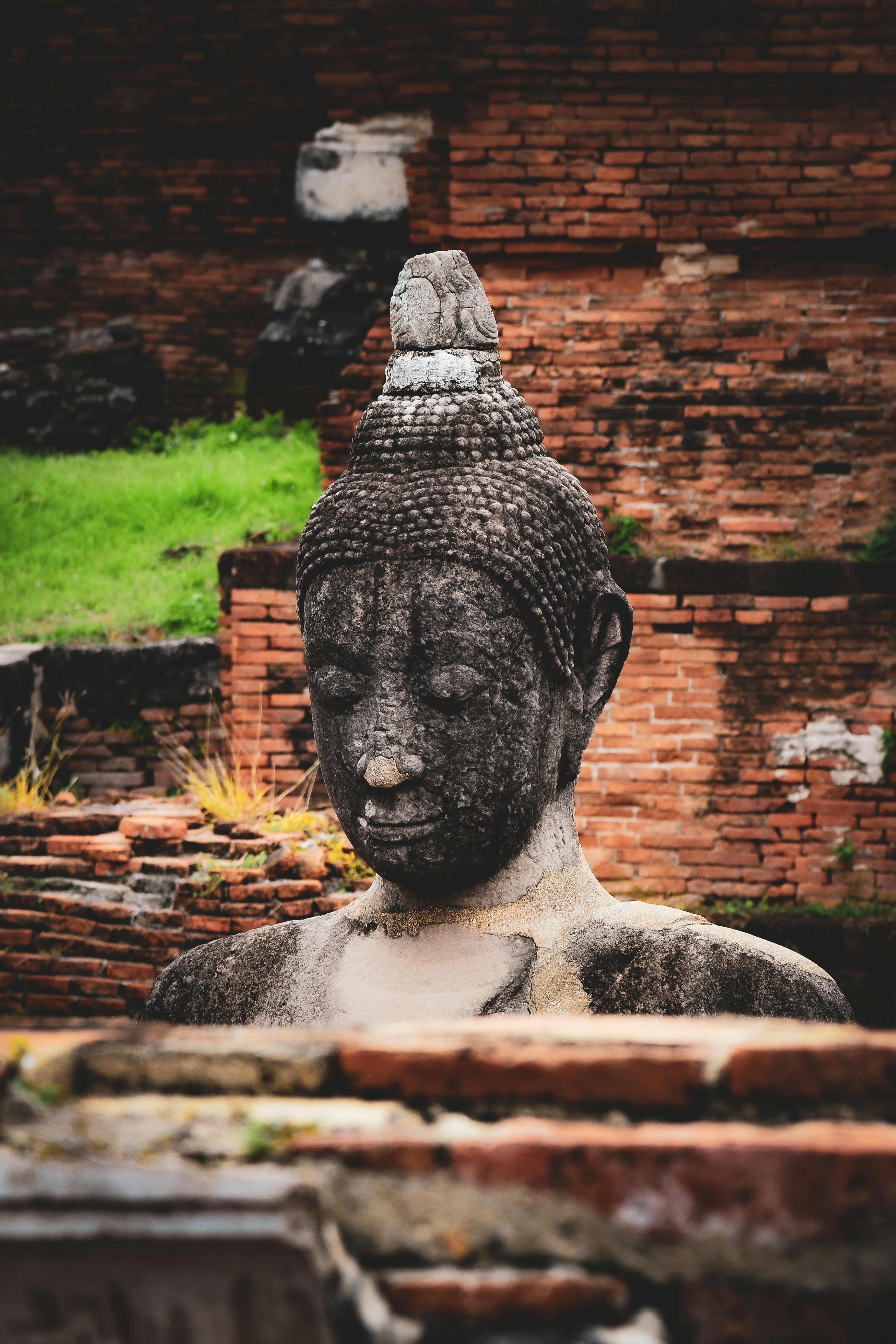 Weathered stone buddha statue amidst ancient brick ruins.