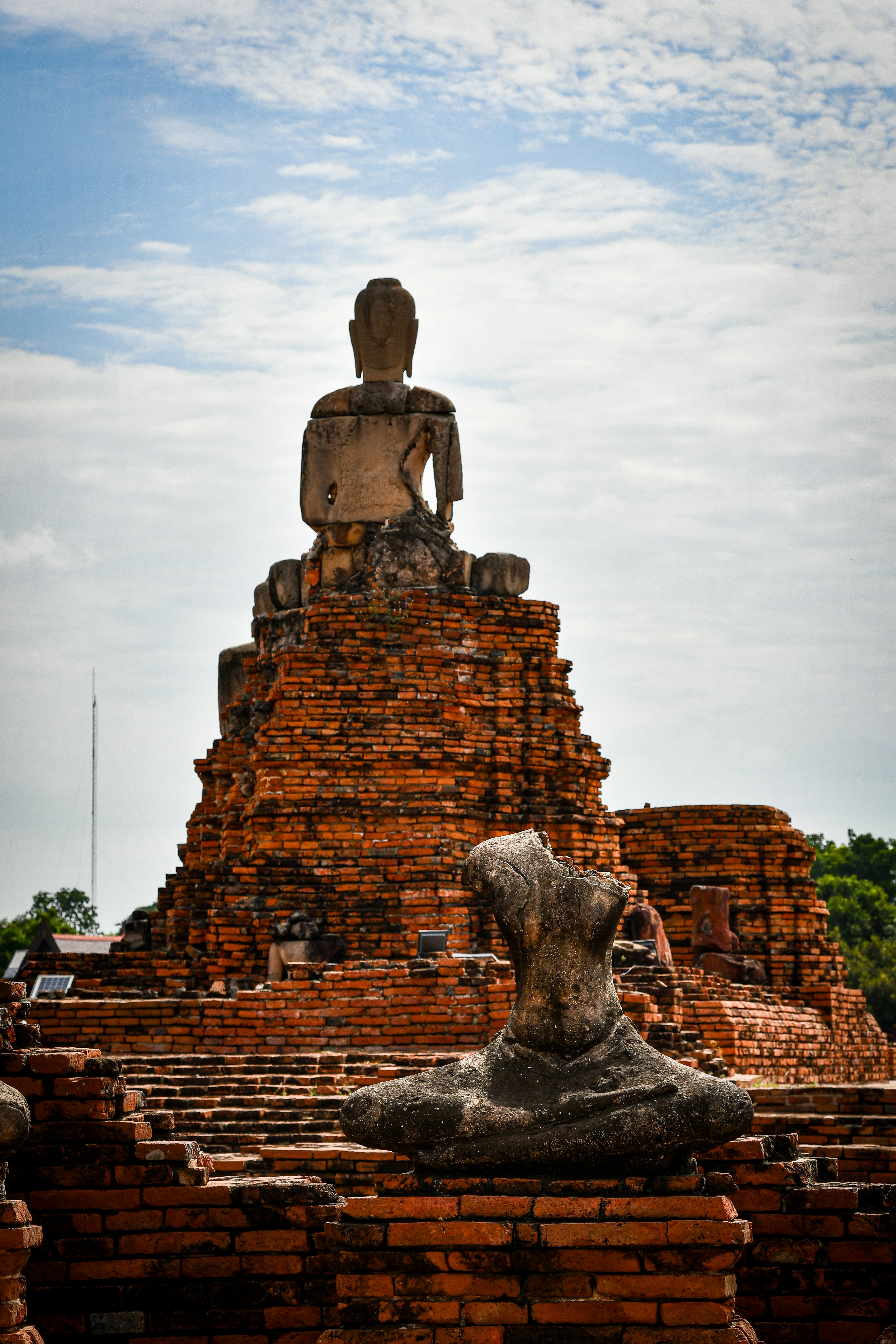 Ancient buddha statues on brick ruins under a cloudy sky.