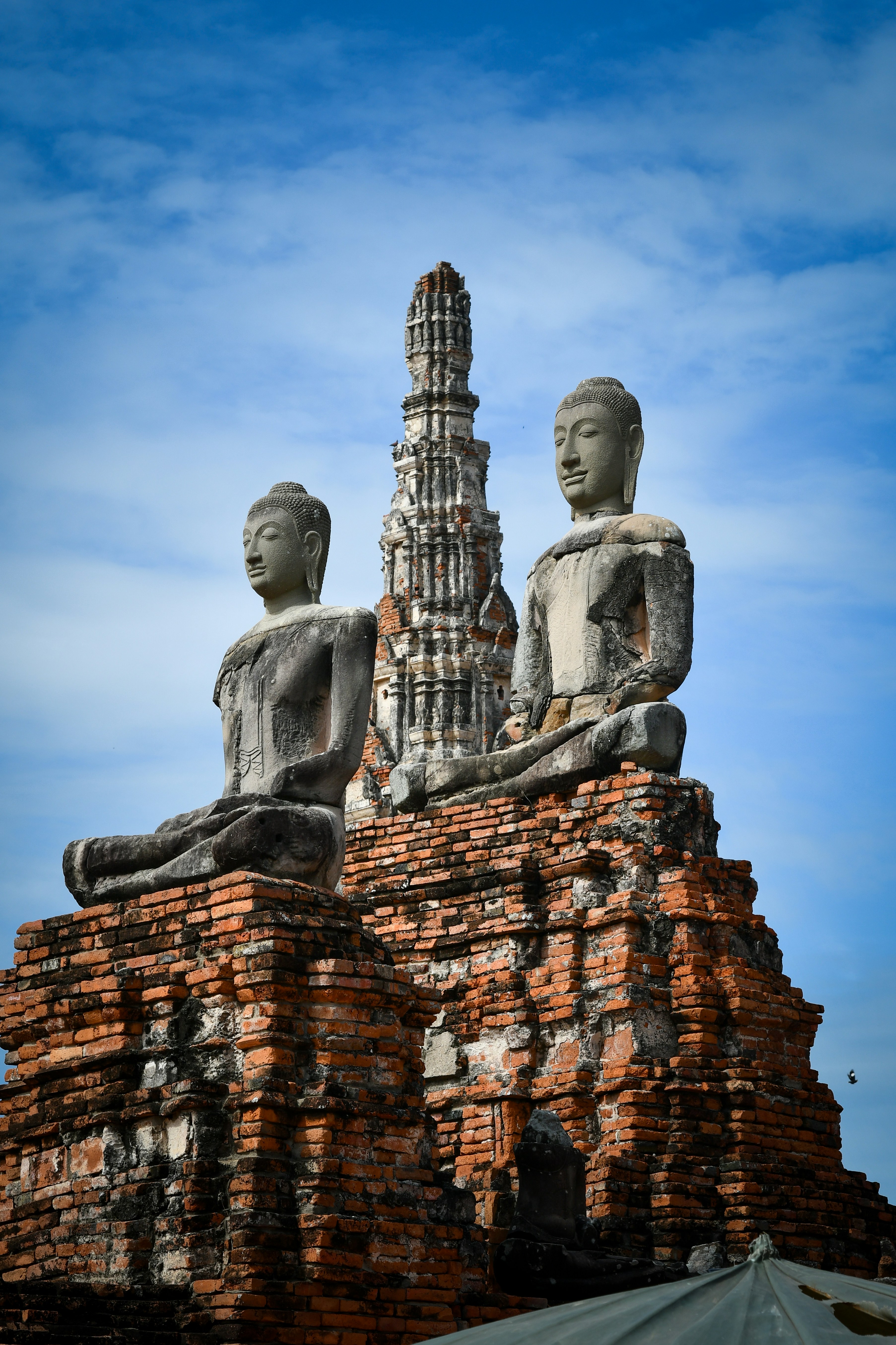 Two ancient buddha statues on brick ruins under blue sky.