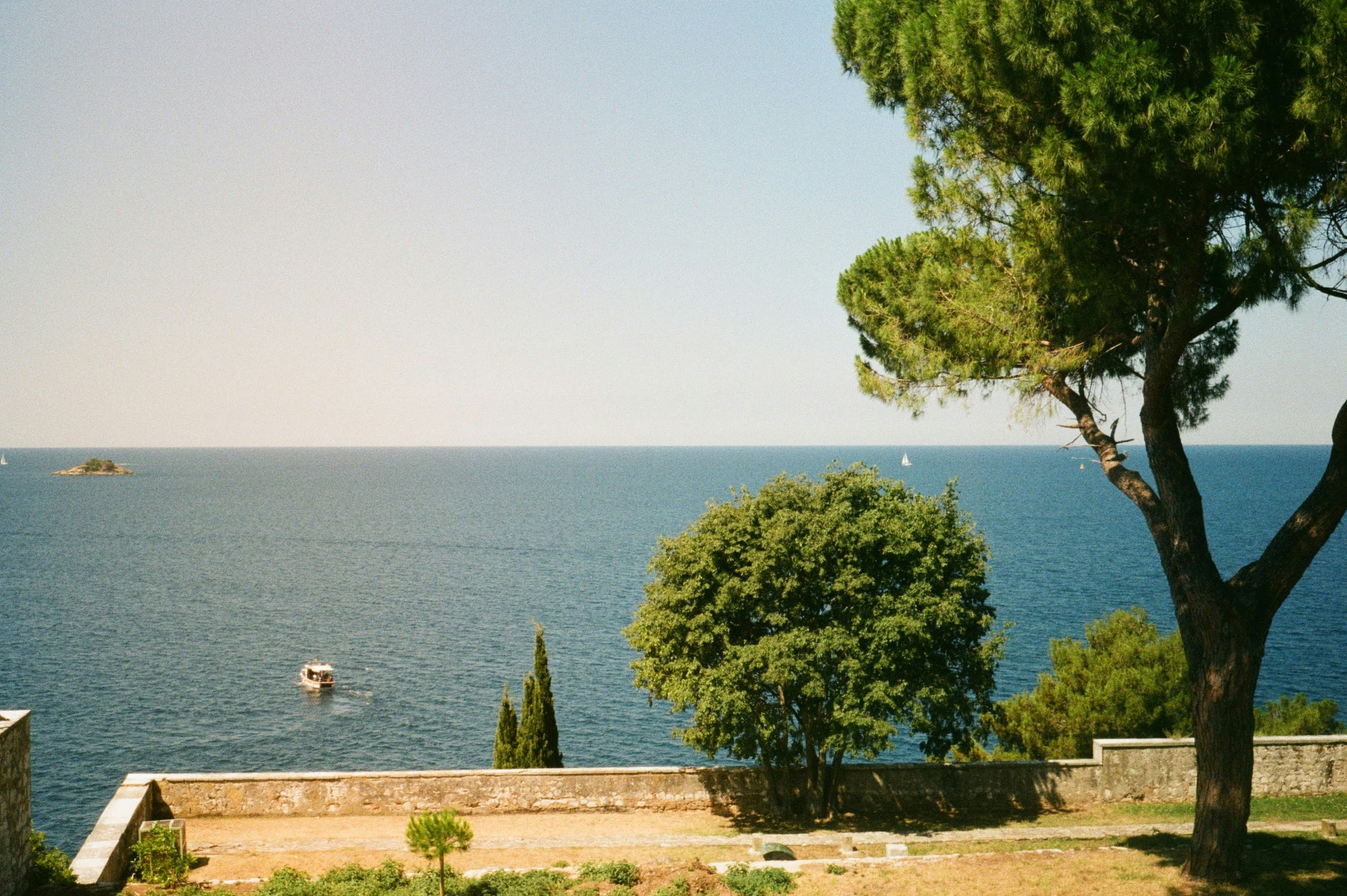 Blue sea view with green trees and a distant boat