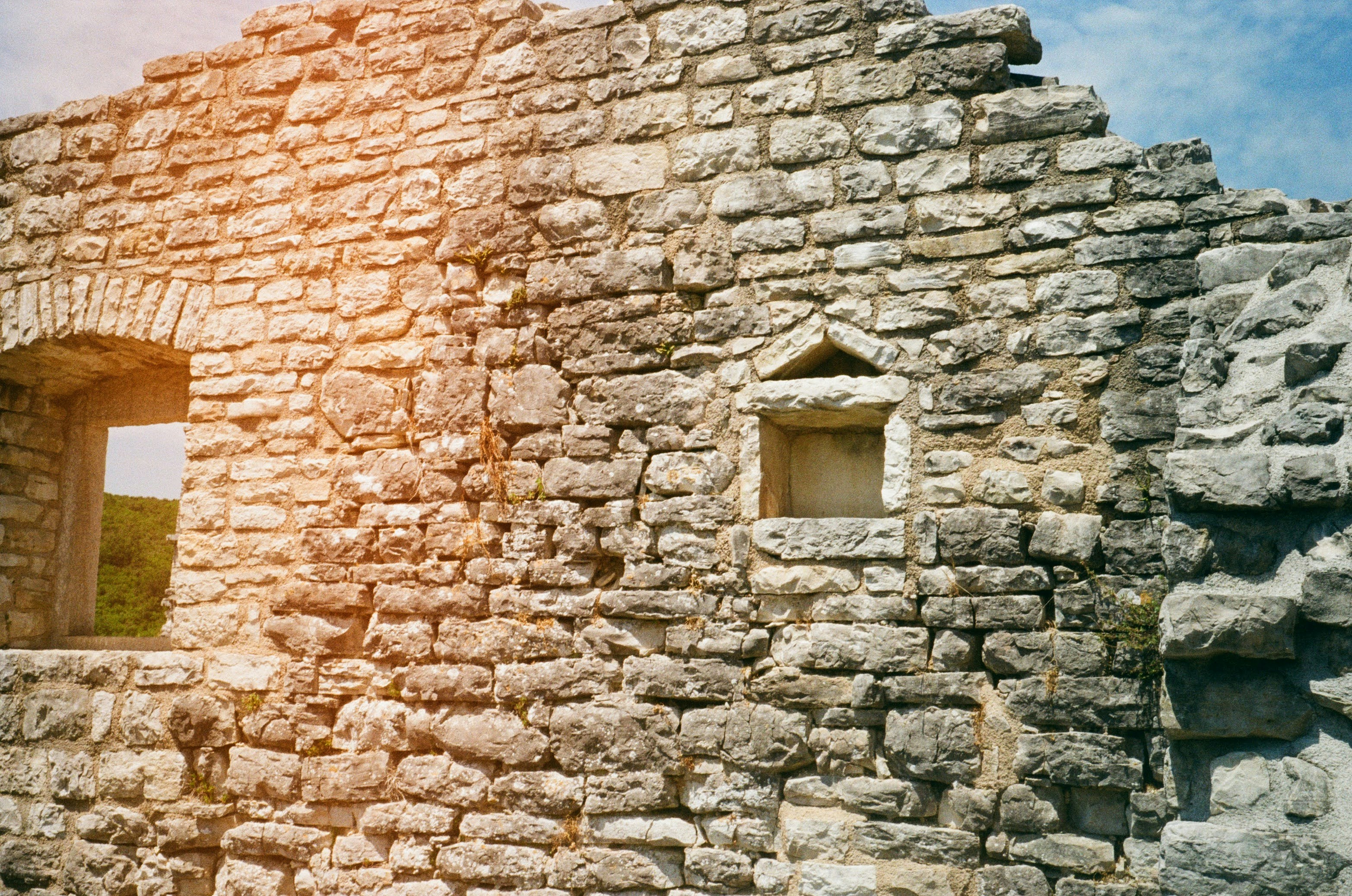 Old stone wall with two windows and warm sunlight.