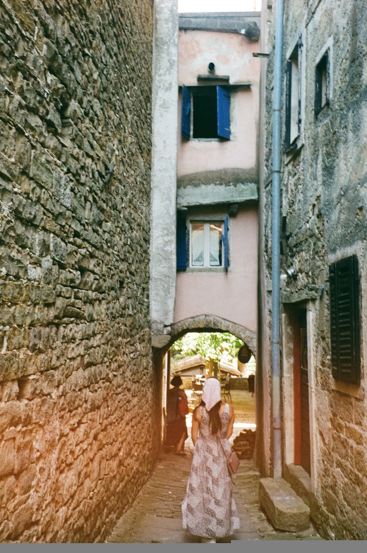 A woman walking down a narrow stone alley toward an arch in Grožnjan