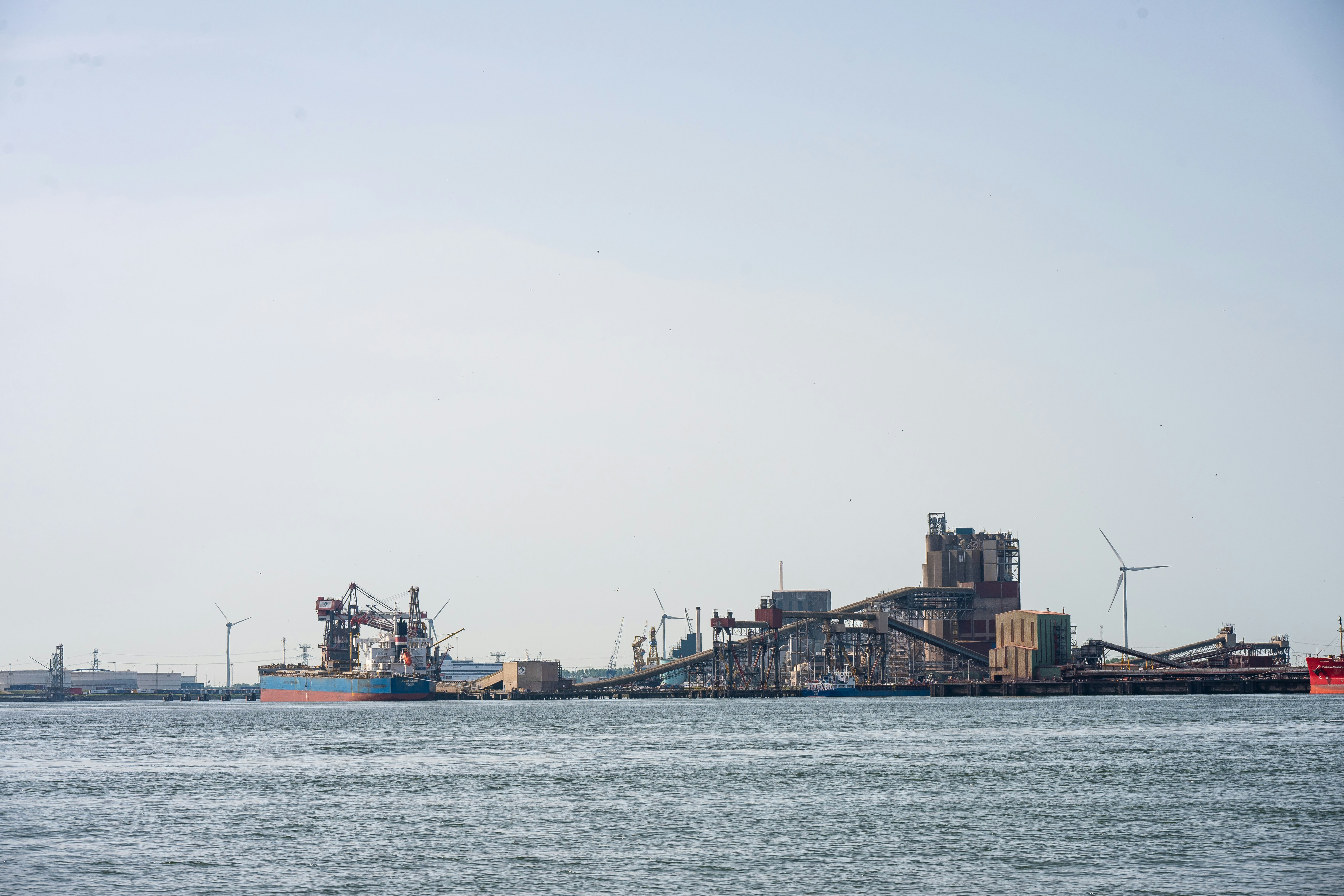Industrial port with cargo ships, silos, and wind turbines