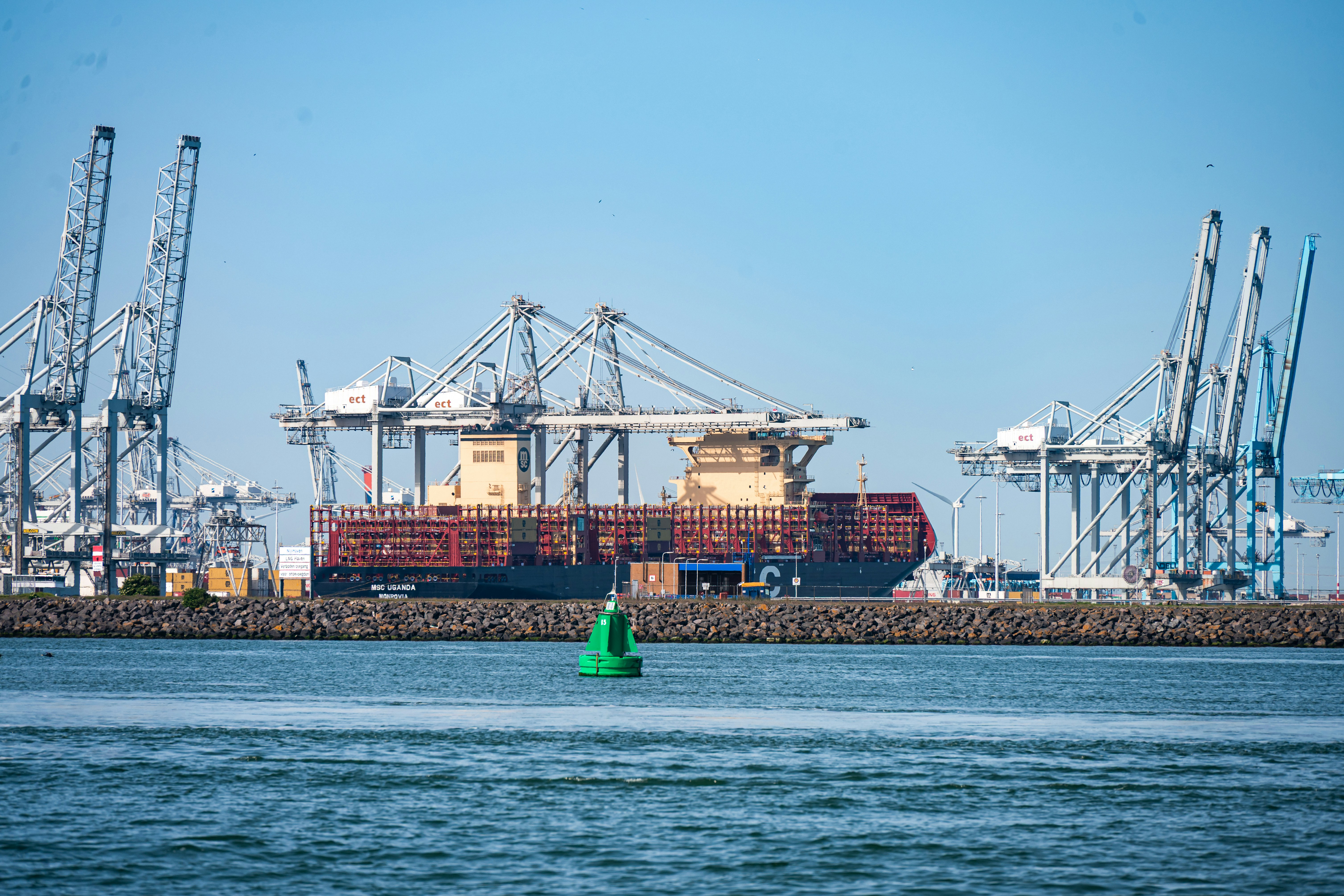 Container ship docked at port with multiple industrial cranes.