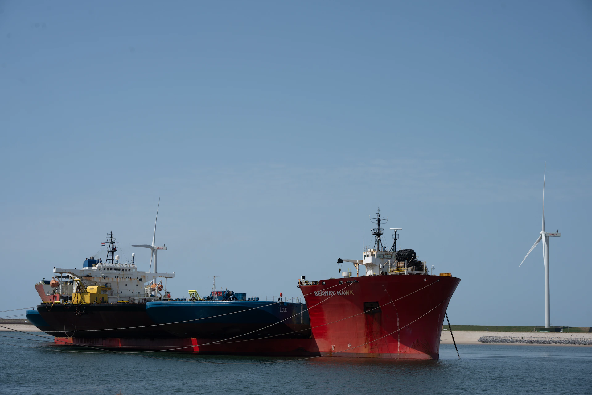 Two cargo ships docked by a wind turbine