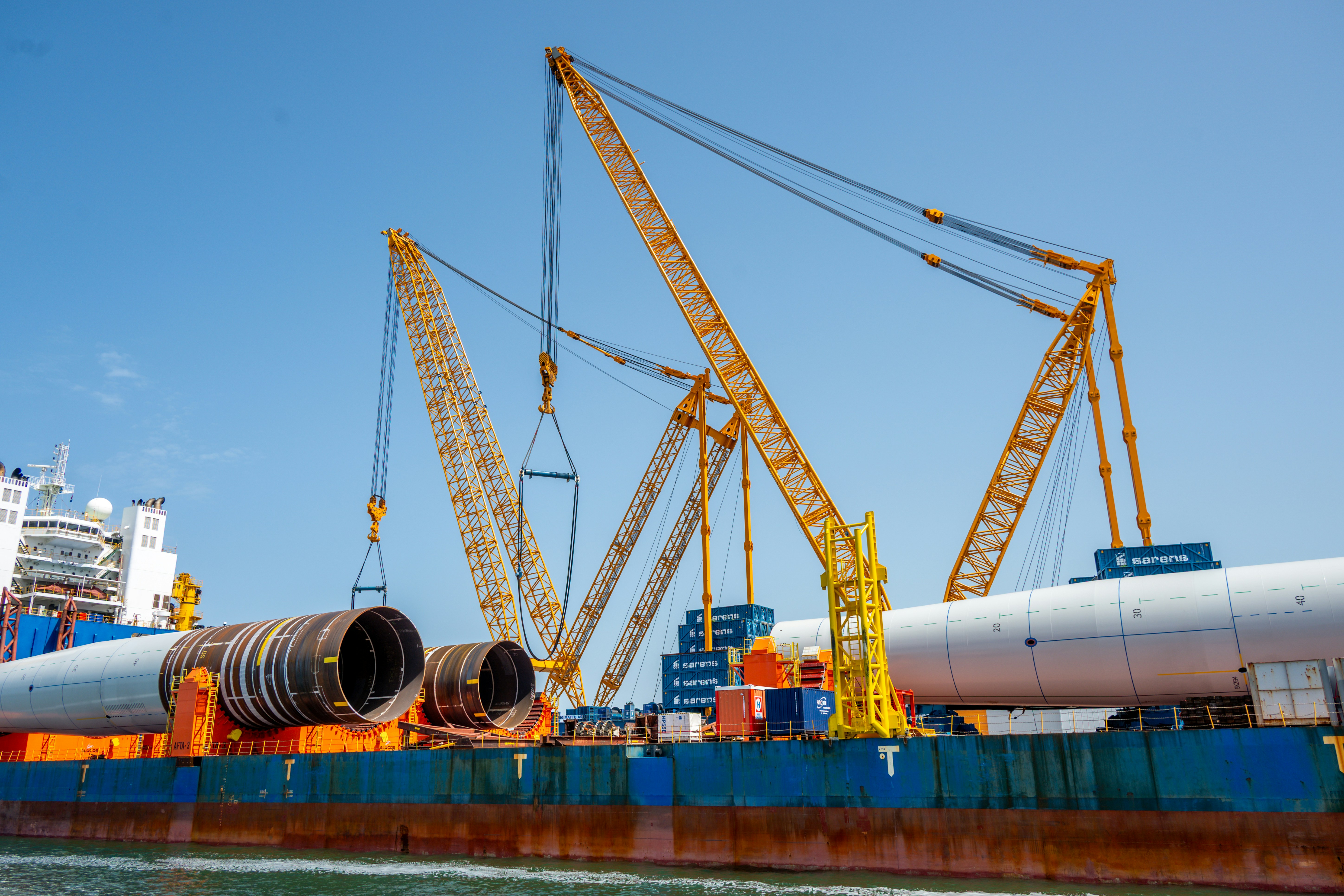 Large cranes lift massive pipes onto a cargo ship