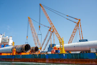 Large cranes lift massive pipes onto a cargo ship