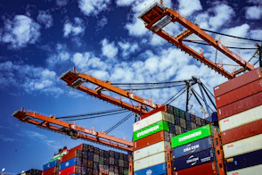 Large shipping cranes and stacked containers against a cloudy sky