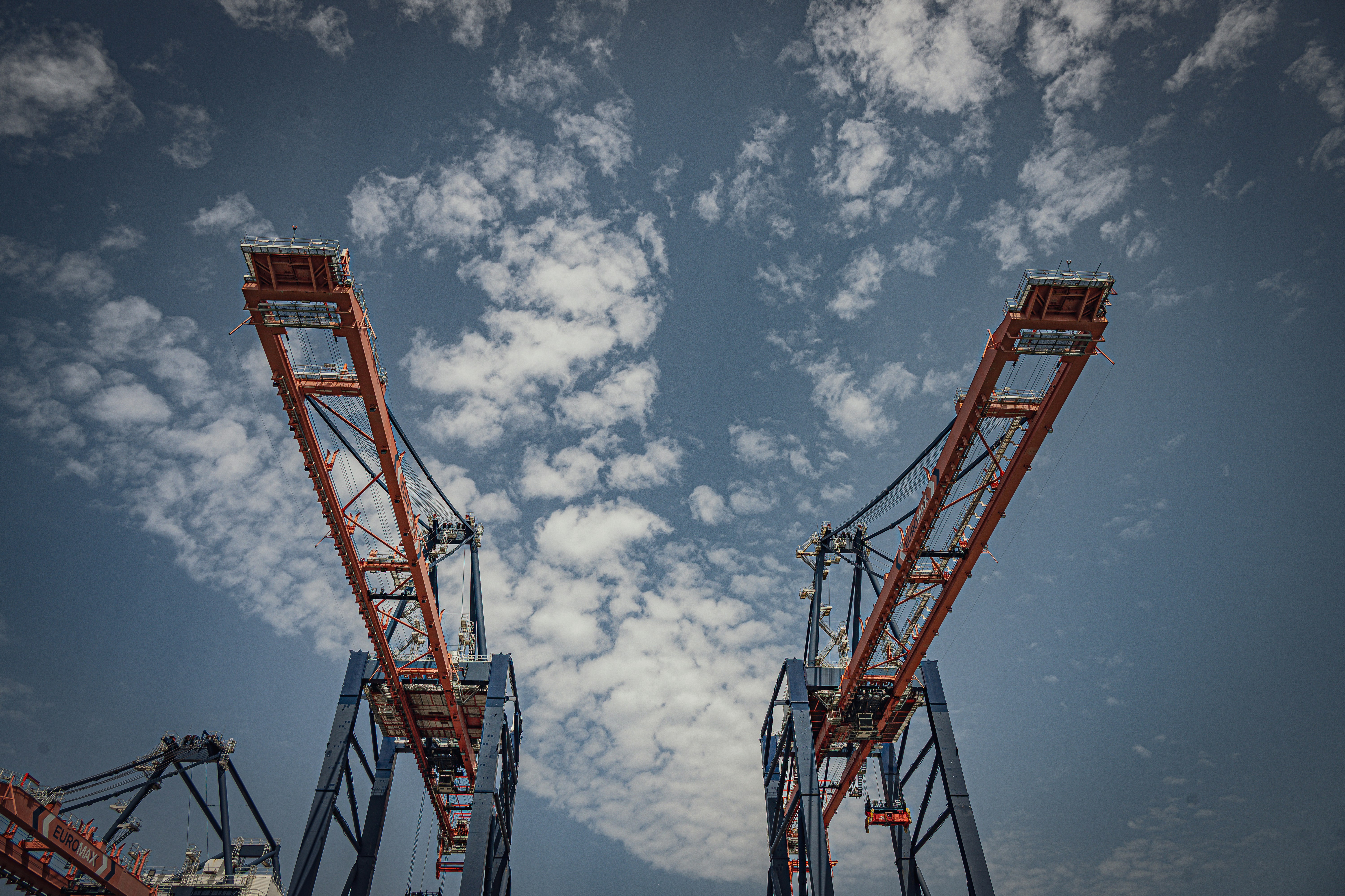 Two large industrial cranes against a cloudy blue sky
