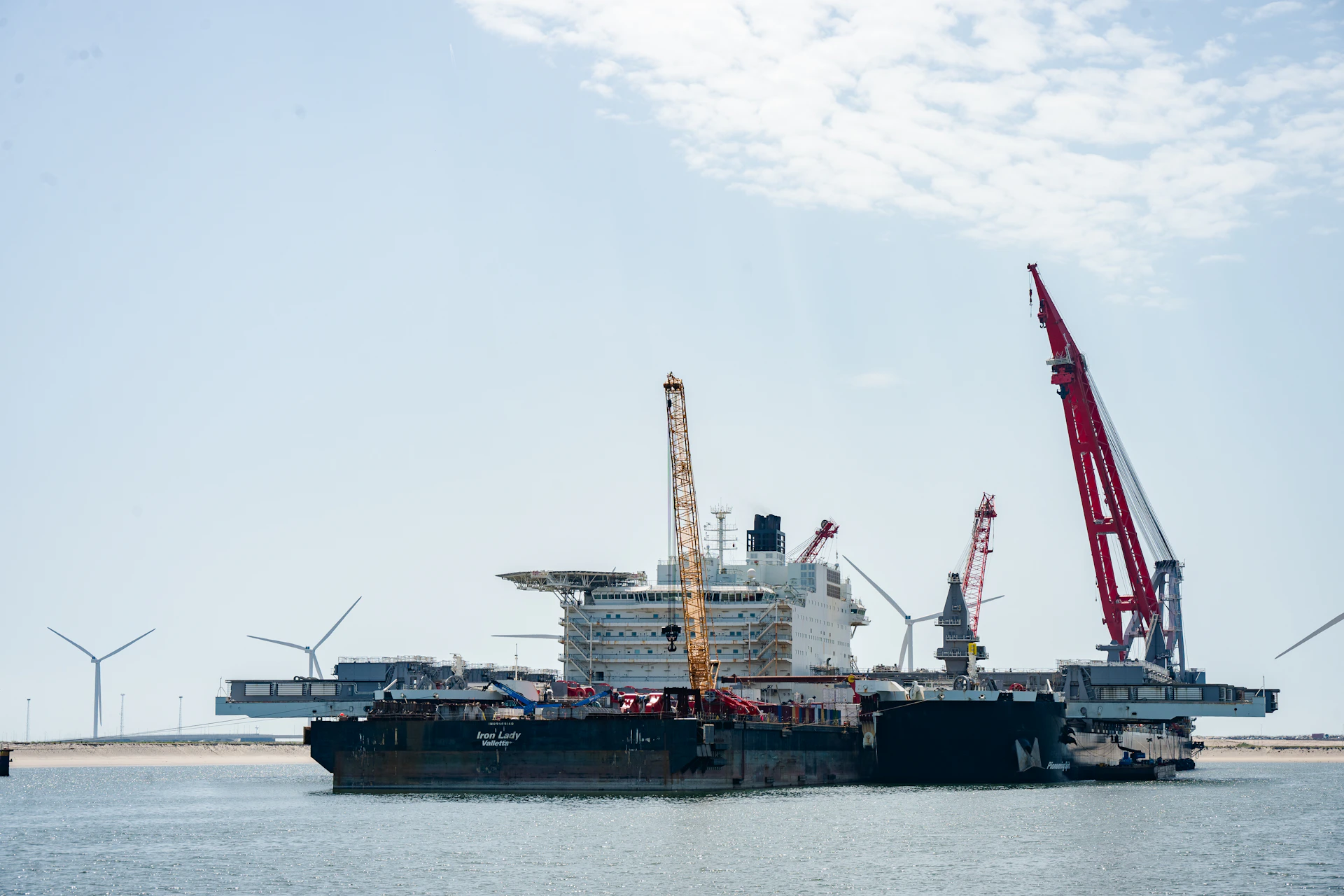 Large offshore vessel under construction with cranes and wind turbines