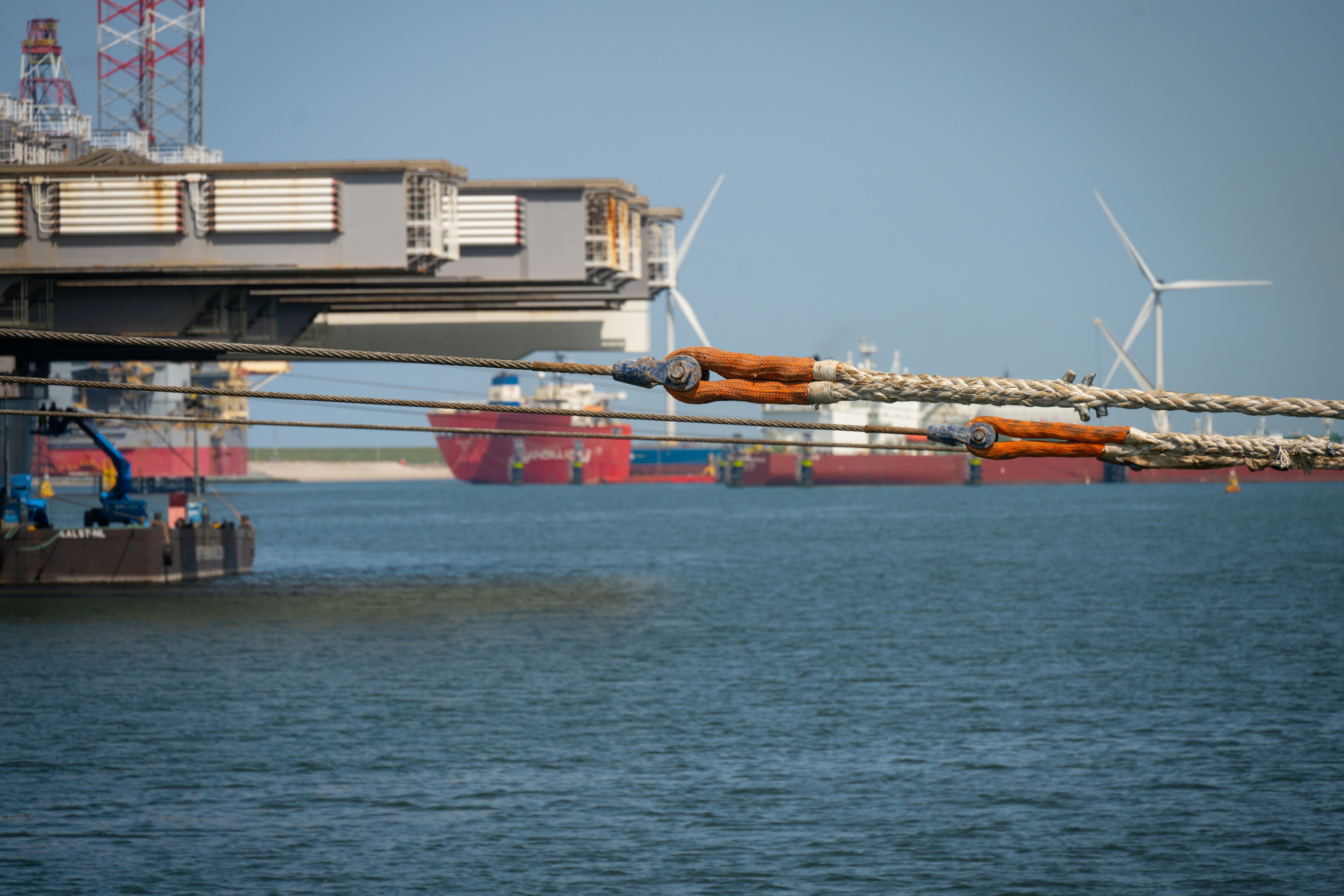Industrial port with ships, large structures, and wind turbines.