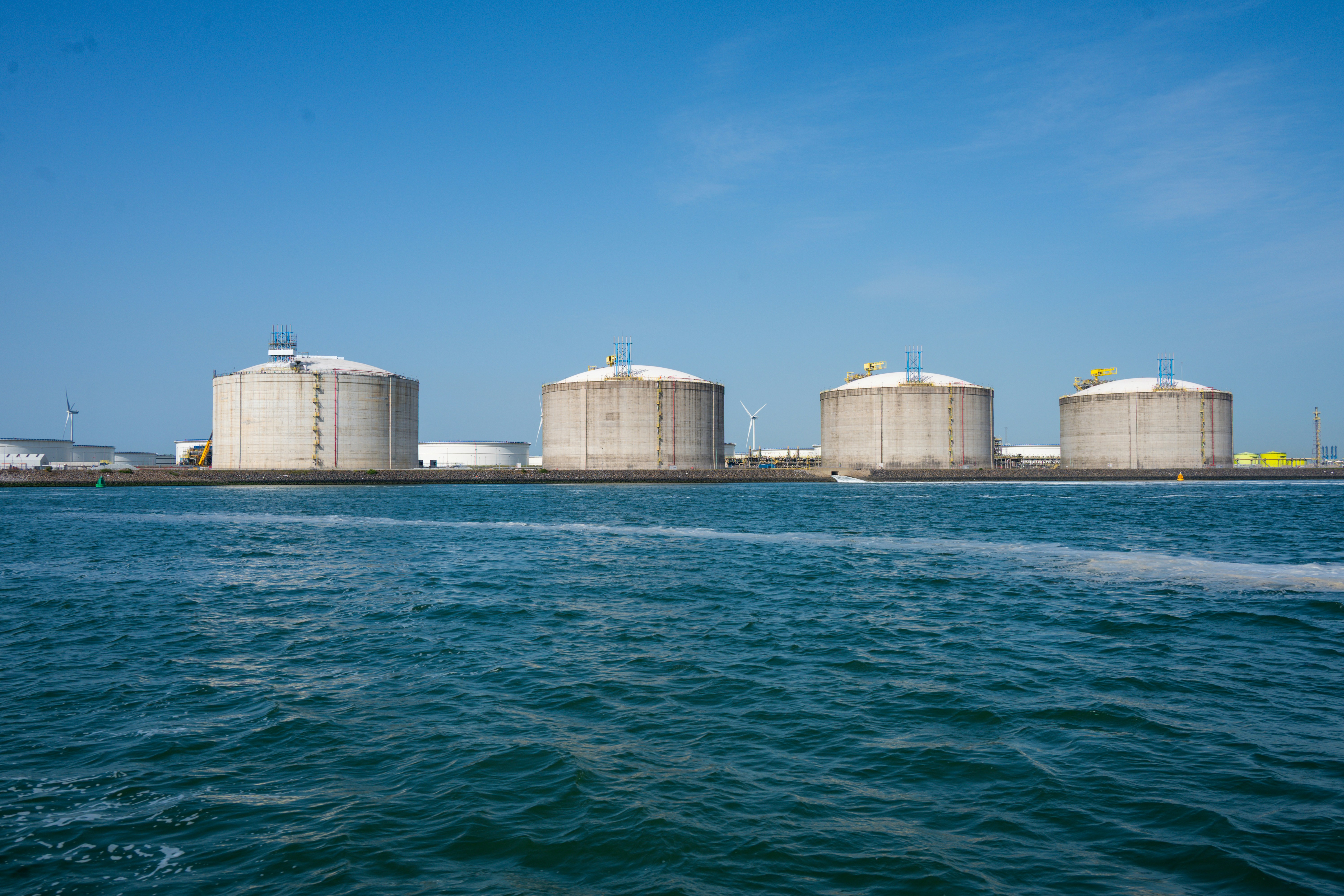 Large industrial gas storage tank farm beside water under clear sky