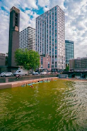 Kayakers paddle on a green urban river with tall buildings