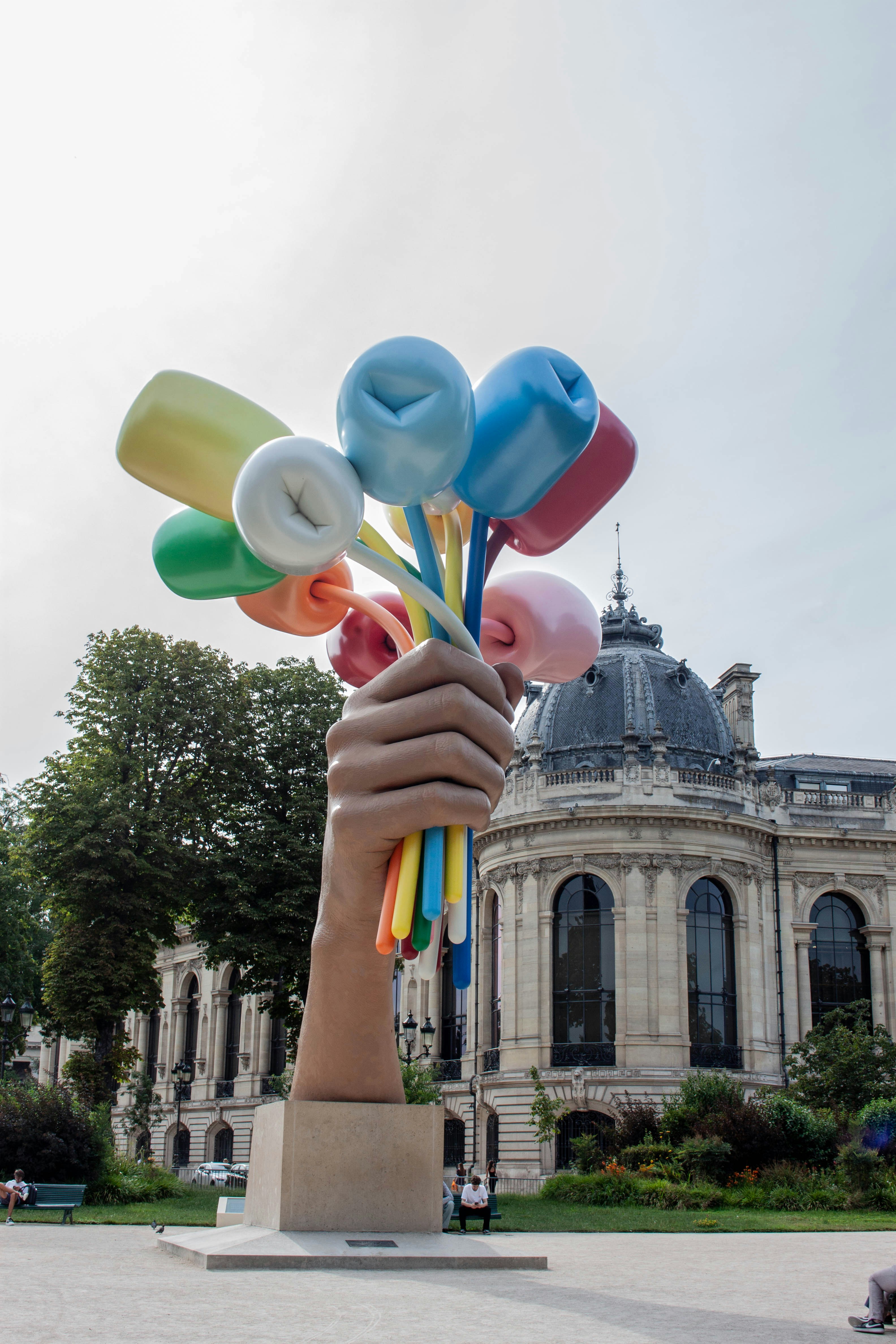 Una gigantesca scultura a mano che tiene palloncini colorati davanti a un edificio classico
