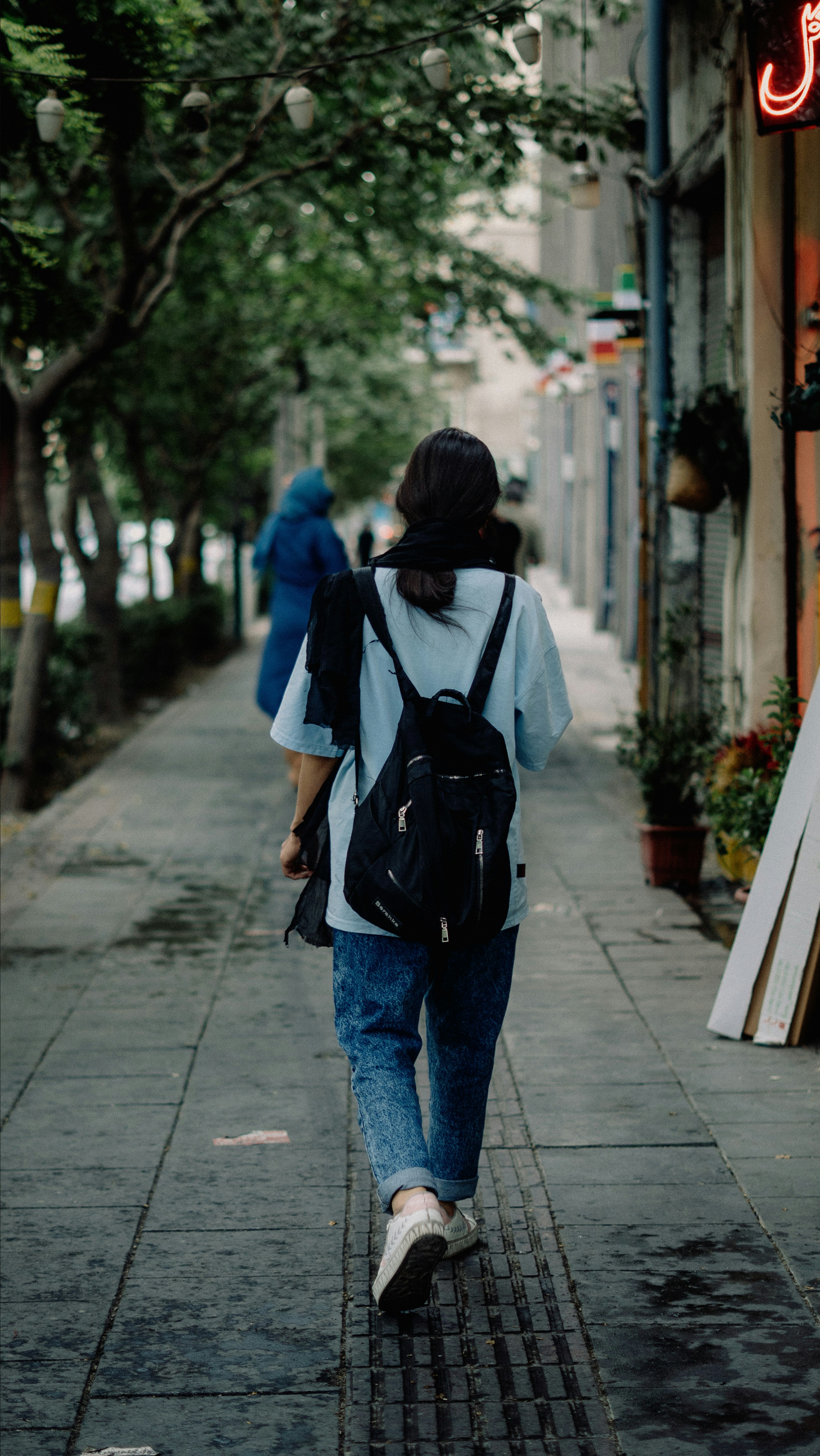 Person with backpack walks down a tree-lined city street.